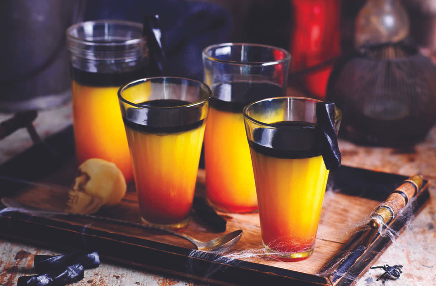 Halloween Cocktails 桌布 壁紙 — 四杯橙色和黑色分層飲料放在一個質樸的木托盤上，配有萬聖節裝飾。
