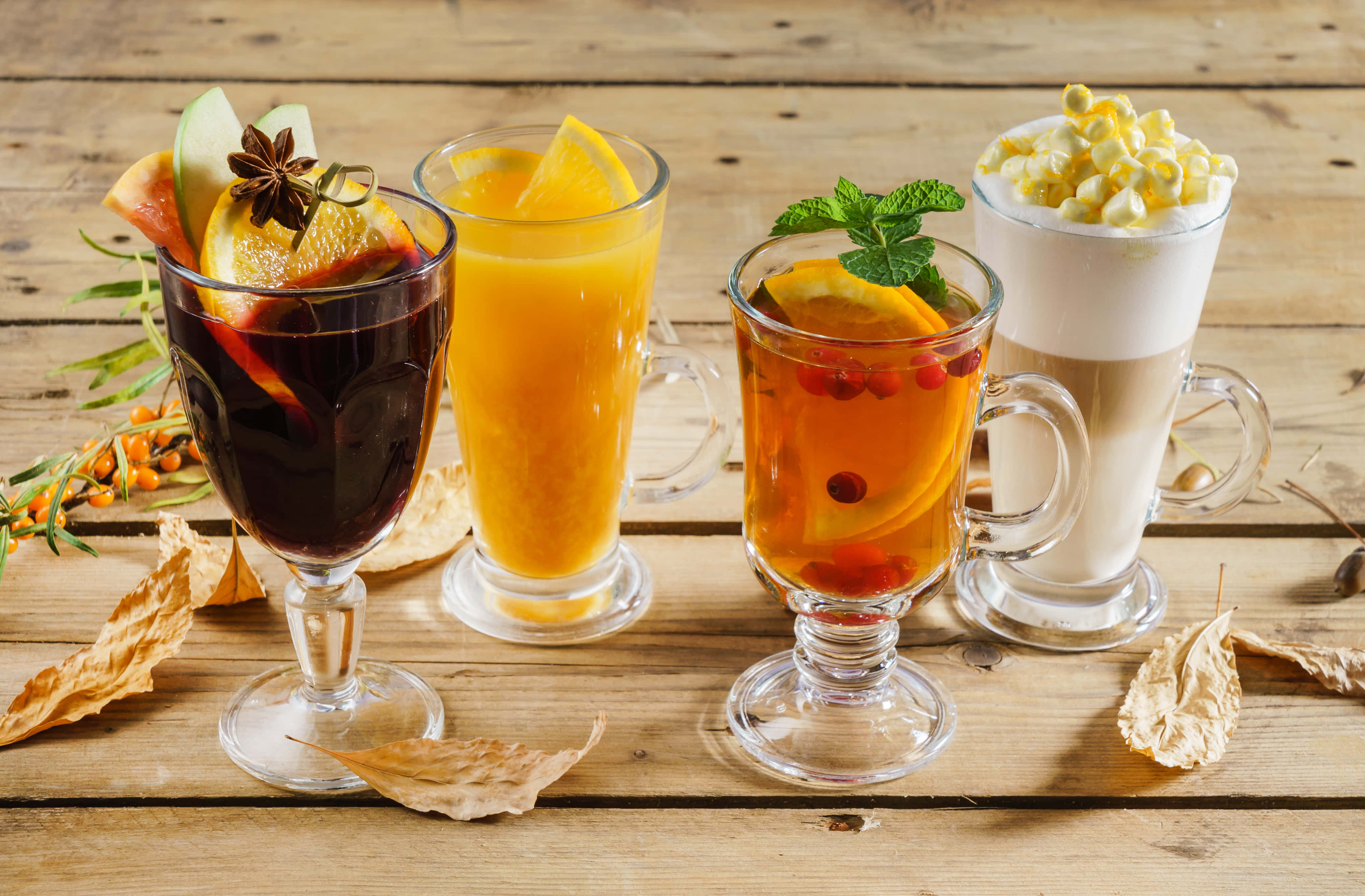 Winter Drinks 桌布 壁紙 — 四杯節日秋季飲品，以水果和香草點綴，放在一張散落著乾燥樹葉的質樸木桌上。