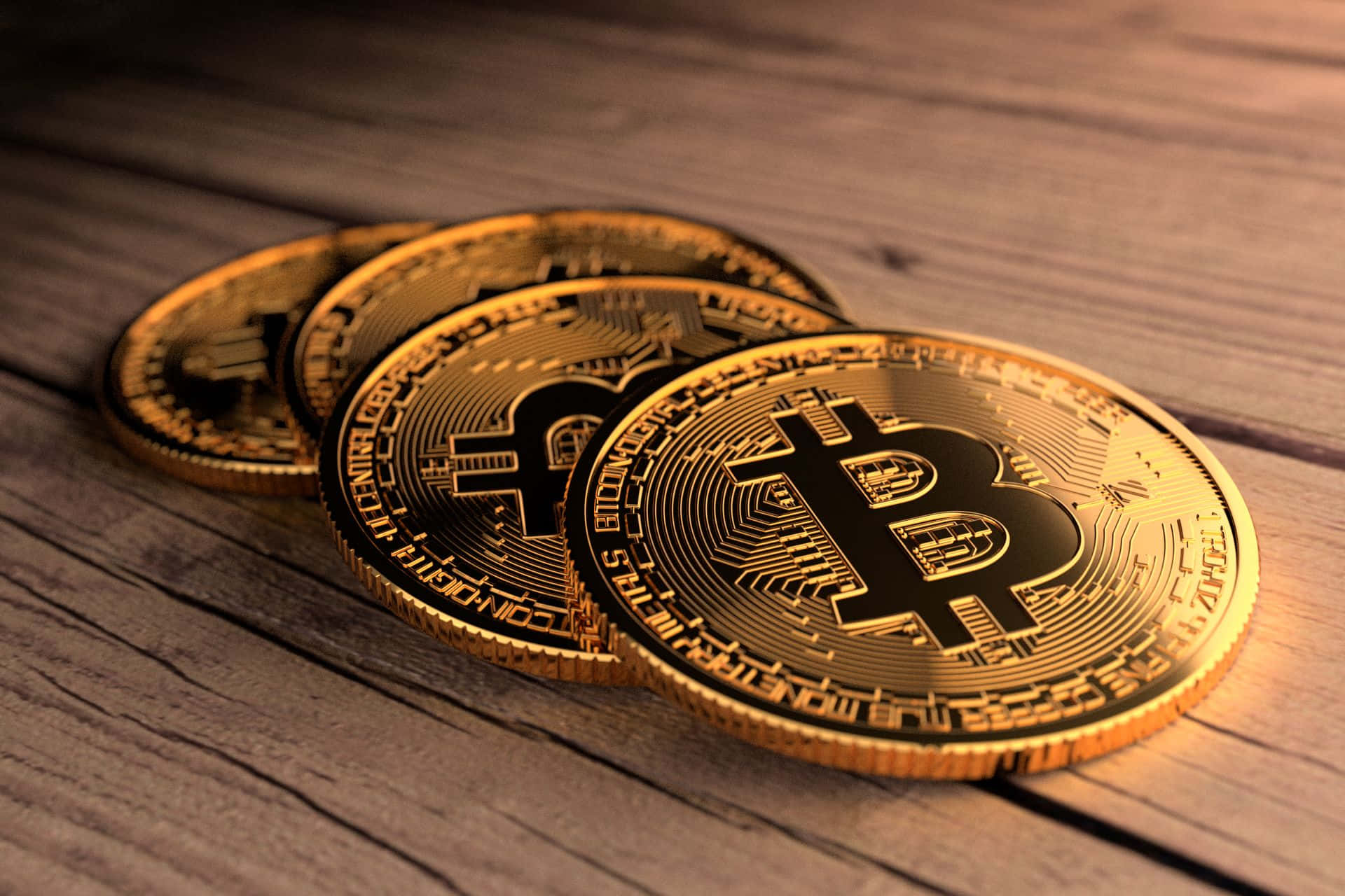 比特幣 桌布 壁紙 — 四枚閃閃發光的金色比特幣以對角線堆疊在經風化的木質表面上，在溫暖的燈光下。