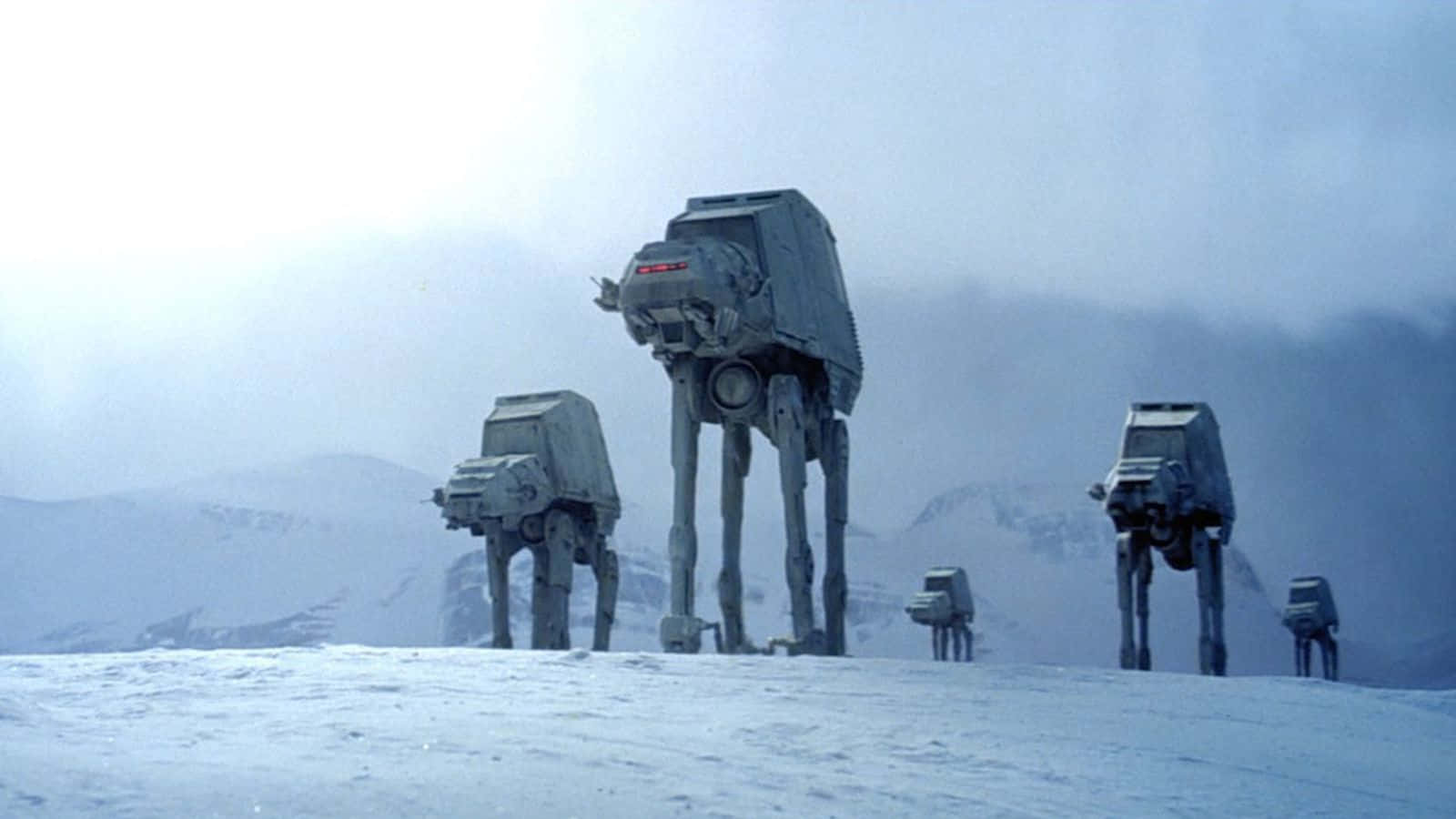 At-at 桌布 壁紙 — 四架AT-AT步行機在陰天之下，穿越白雪覆蓋的山地景觀。