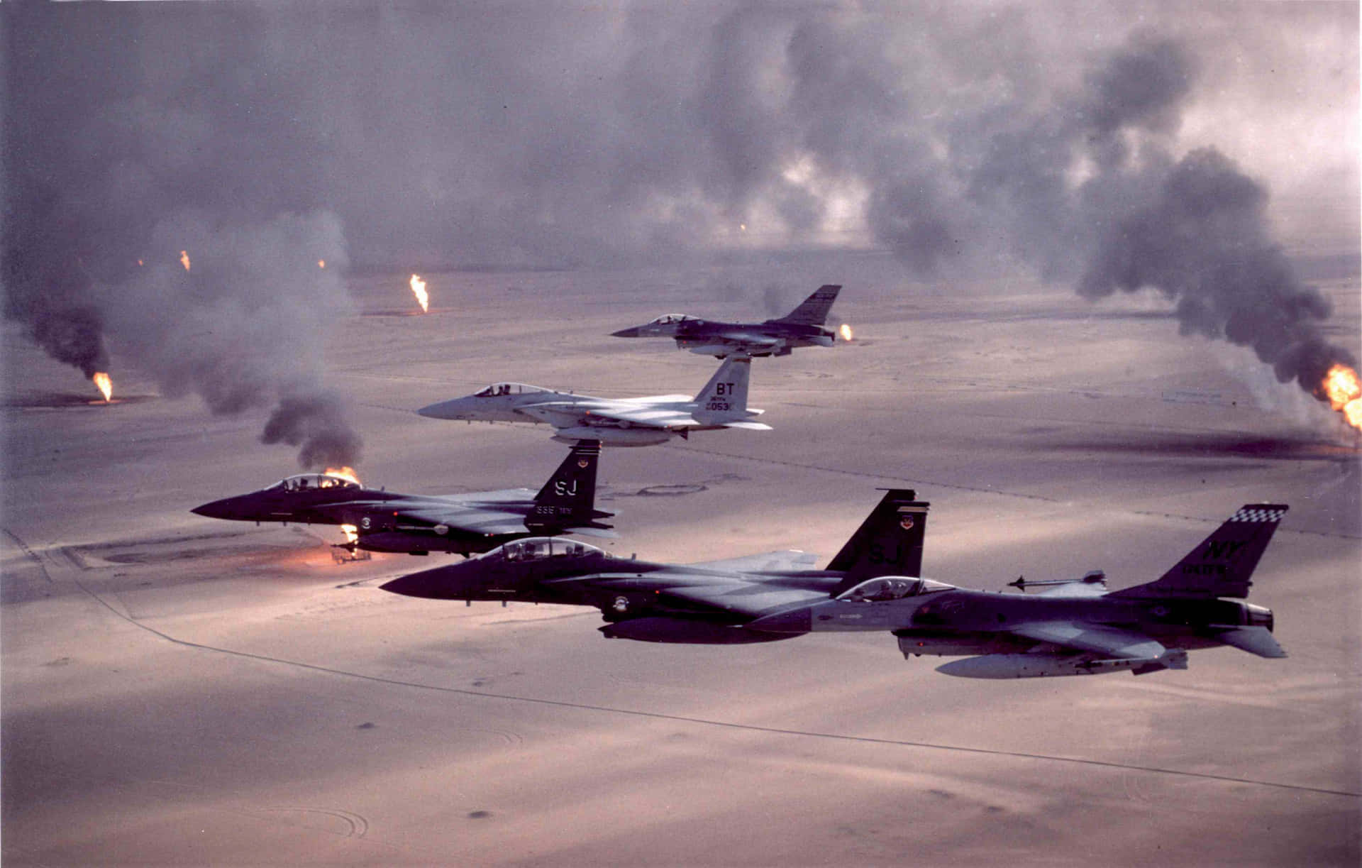 Military Plane 桌布 壁紙 — 四架戰鬥機低飛過一個被下方爆炸產生的濃煙和火焰吞沒的沙漠機場。