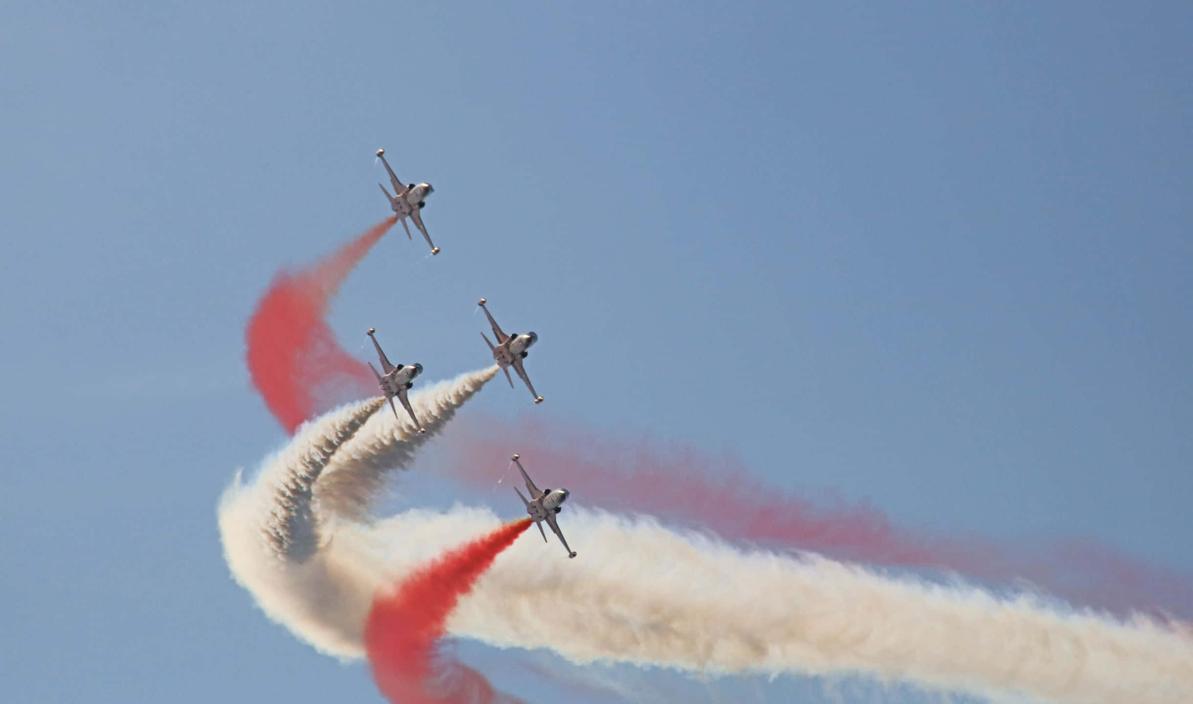 2440x1440 Small Planes 桌布 壁紙 — 四架戰鬥機在晴朗的藍天中以緊密編隊翱翔，留下鮮豔的紅色和白色煙霧痕跡。