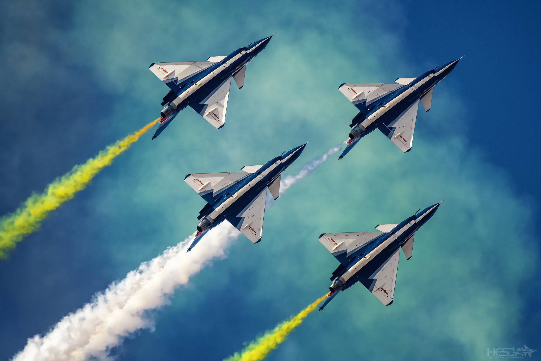 Air Force 桌布 壁紙 — 四架戰鬥機在鮮豔的藍天中緊密編隊飛行，留下鮮明的黃色和白色煙跡。