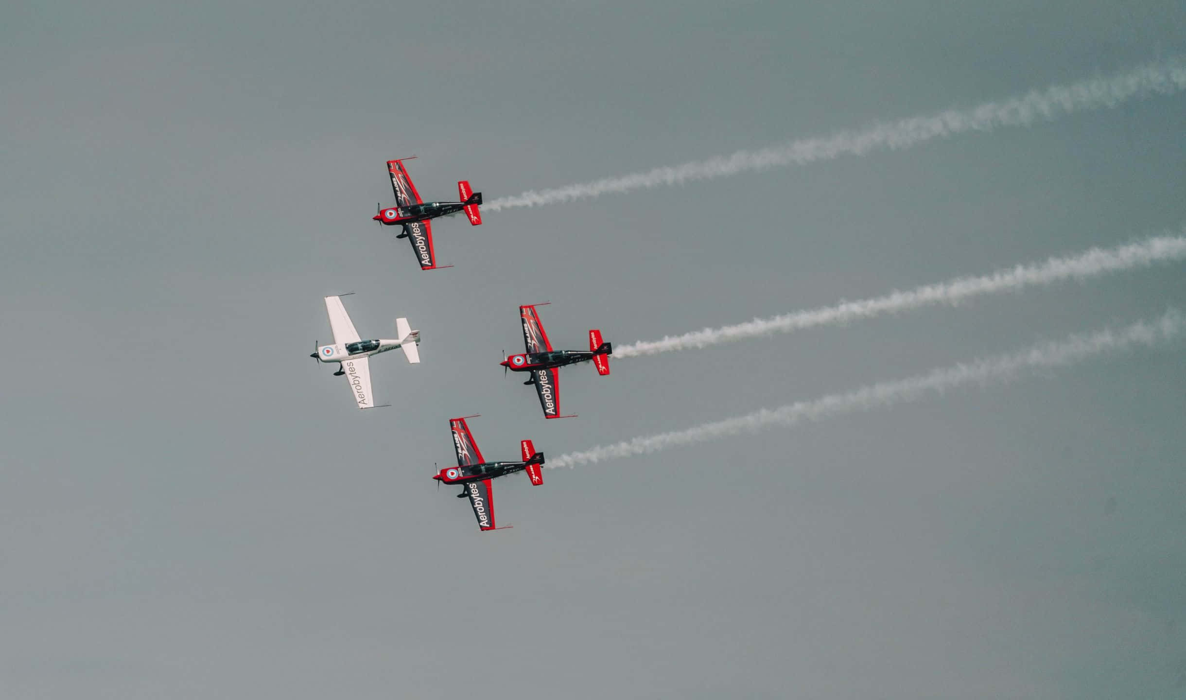 2440x1440 Small Planes 桌布 壁紙 — 四架特技飛機在灰色天空下緊密編隊飛行，留下白色煙霧痕跡。