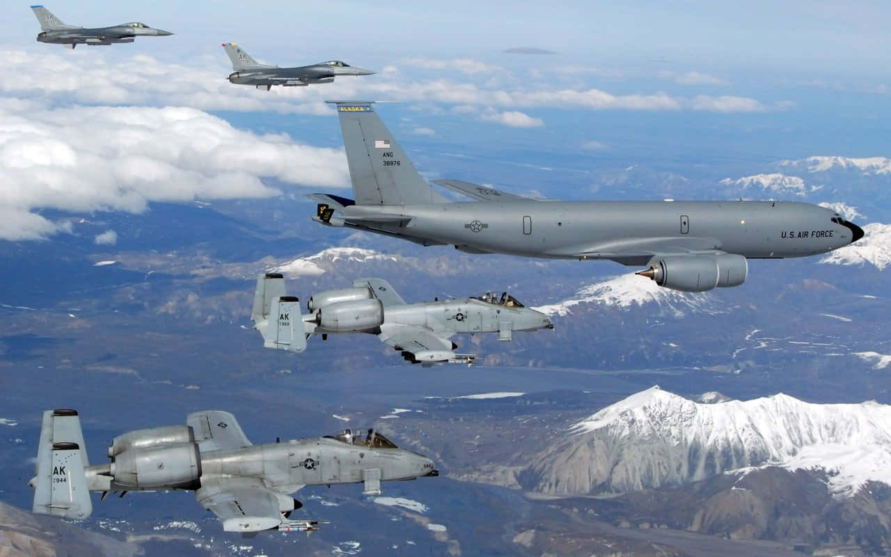  壁紙 — 四架美國空軍戰鬥機在部分多雲的天空下，以編隊飛行於積雪覆蓋的山脈之上。