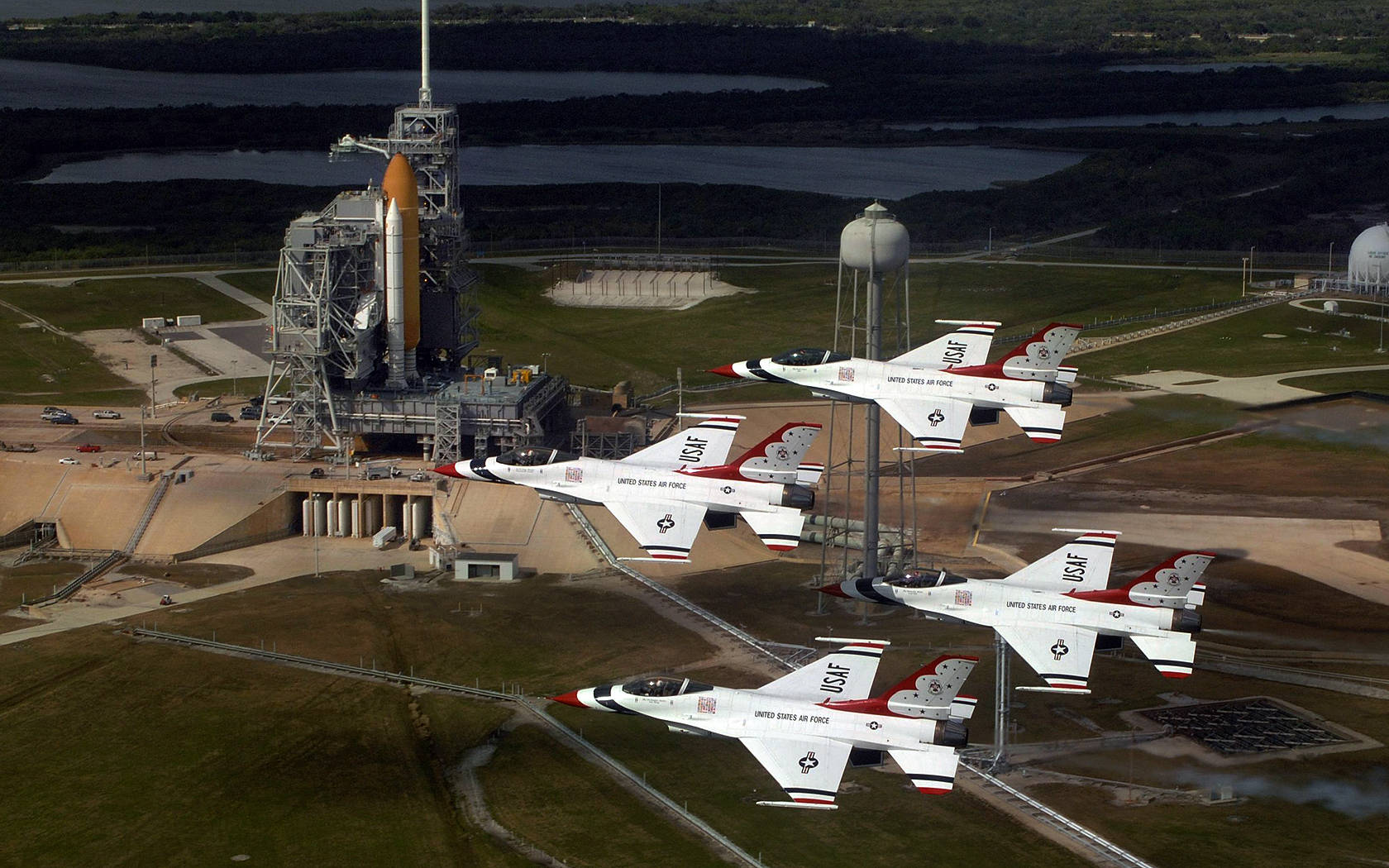 Houston 桌布 壁紙 — 四架美國空軍雷鳥噴射機以緊密編隊飛越NASA發射台，背景有火箭和水塔。