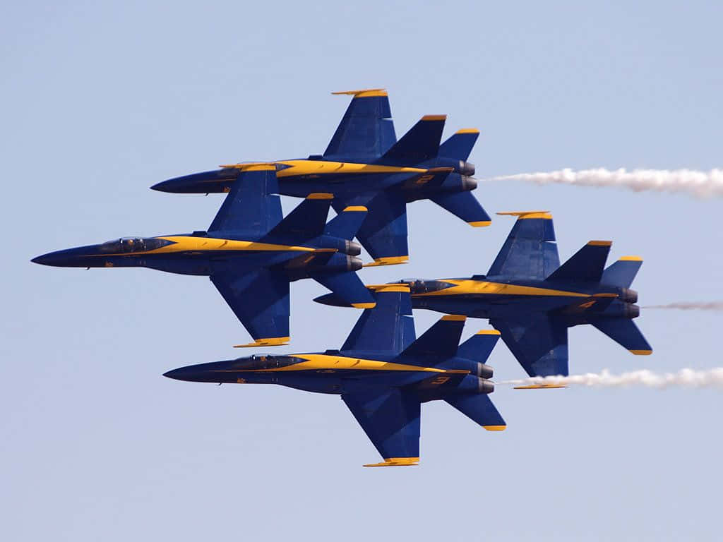 US Navy 桌布 壁紙 — 四架藍黃色戰鬥機在晴朗的天空下以緊密編隊飛行，留下白色煙跡。
