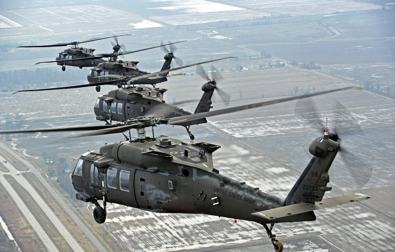 Air Force 桌布 壁紙 — 四架軍用直升機在白雪覆蓋的鄉村景觀上空編隊飛行，下方有道路和田野。