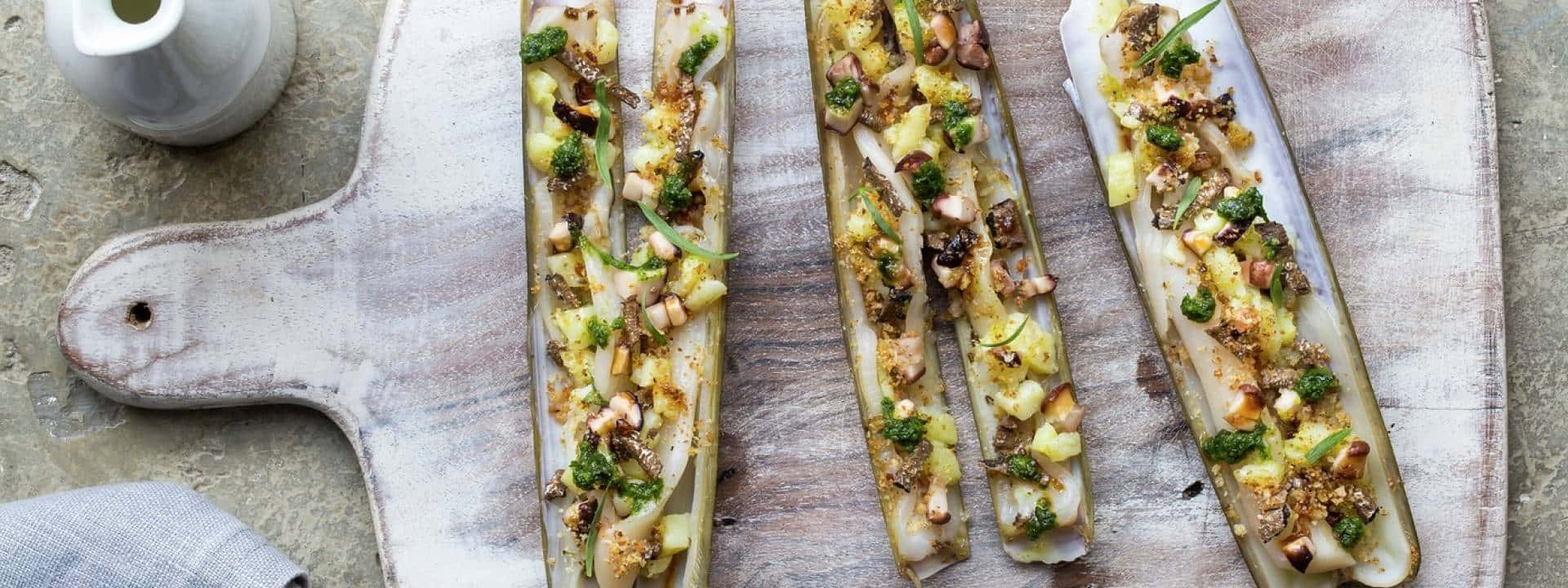 Razor Clam 桌布 壁紙 — 四根烤茴香莖，上面撒上松子、烤香草和切碎的青蔥，放在一個質樸的木砧板上。