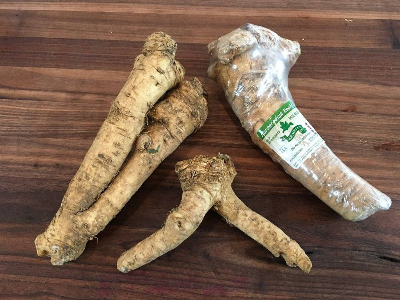 Healthy Food 桌布 壁紙 — 四條帶粗糙米色外皮的生牛蒡根放在深色木質表面上，其中一條用帶綠色標籤的塑膠包裹著。