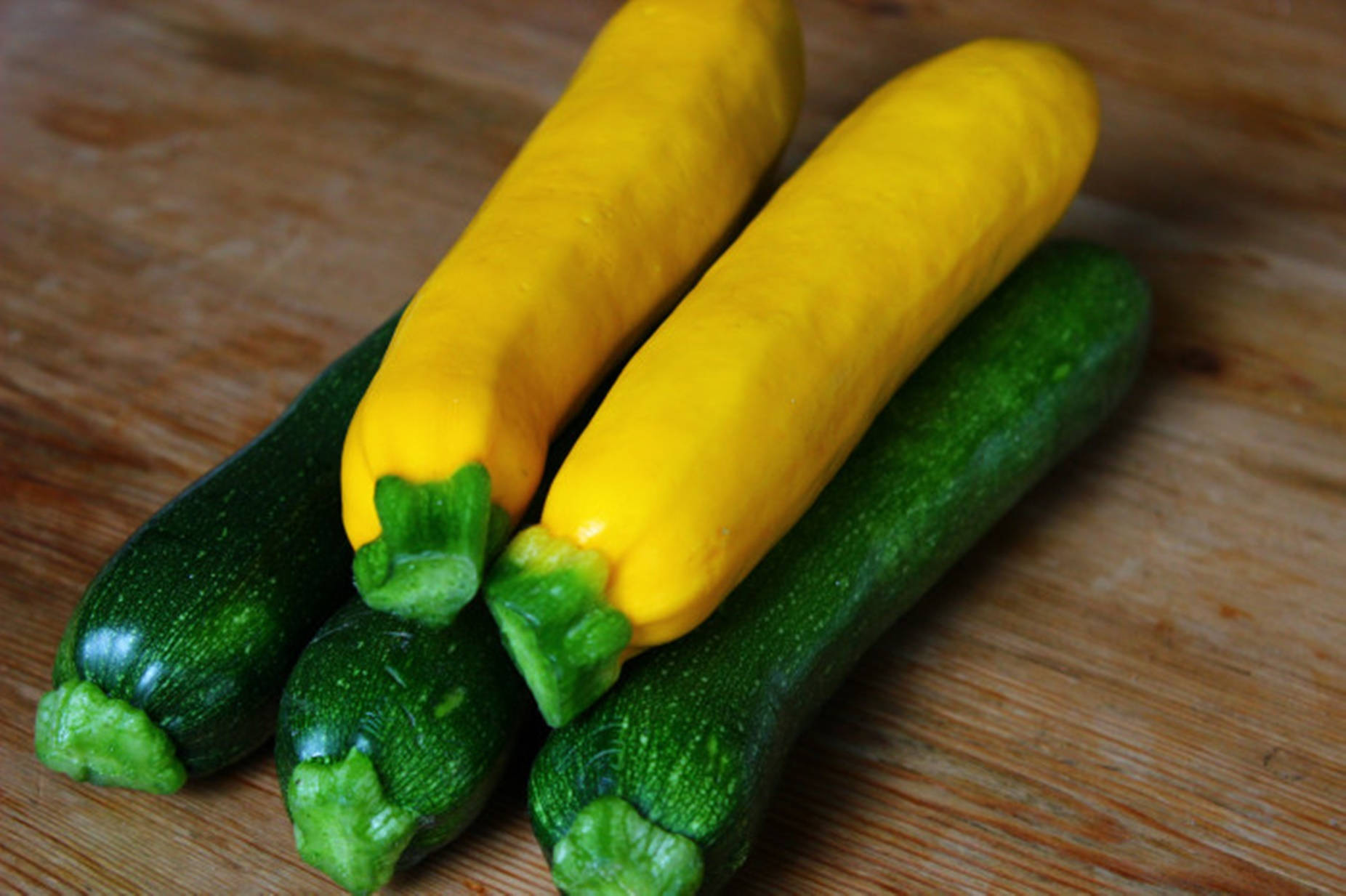 Vegetables 桌布 壁紙 — 四條新鮮櫛瓜，兩條黃色兩條綠色，放在溫暖的木砧板上。