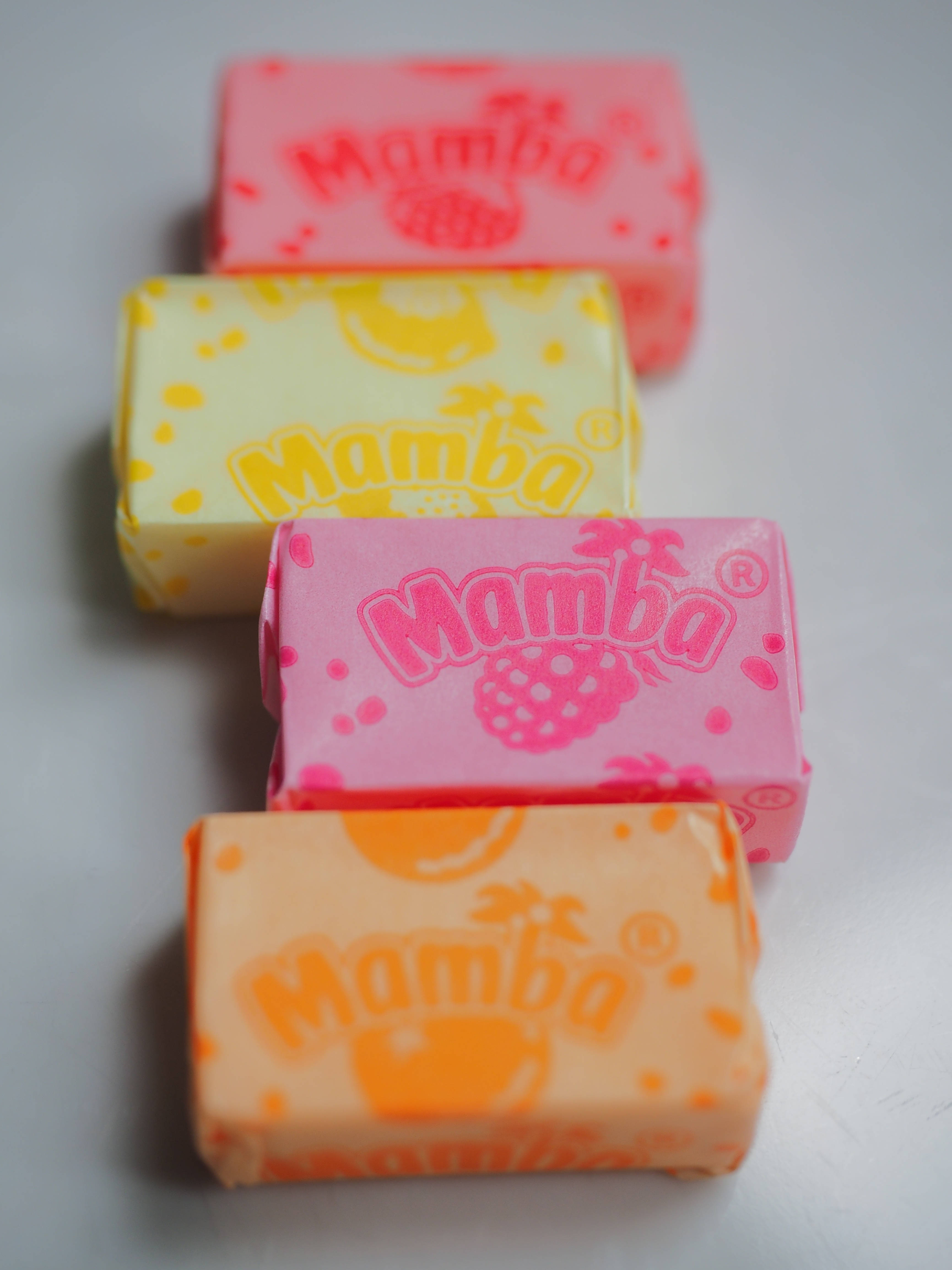 chewy 桌布 壁紙 — 四條色彩繽紛的Mamba糖果棒，包裝分別為粉紅色、黃色、橙色和蜜桃色，以對角線排列在純白色表面上。
