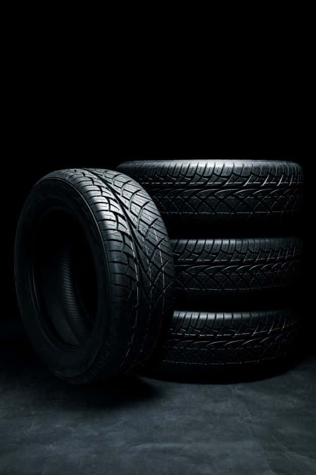 Winter Tires 桌布 壁紙 — 四條黑色汽車輪胎在昏暗光線下堆疊，背景黑暗，帶有戲劇性的陰影。