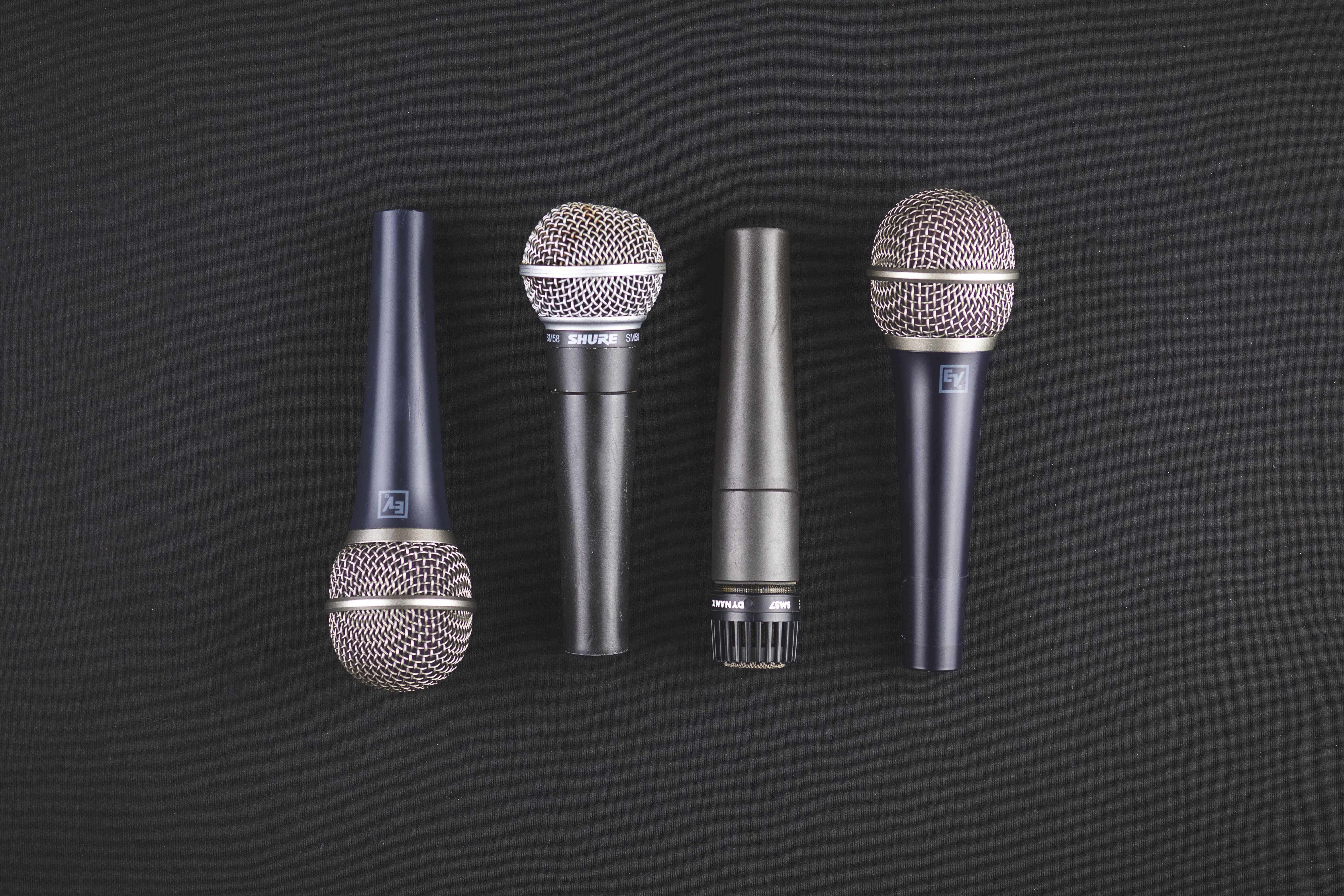 Microphones 桌布 壁紙 — 四款專業麥克風，採用時尚金屬和深藍色飾面，整齊排列在帶紋理的黑色背景上。