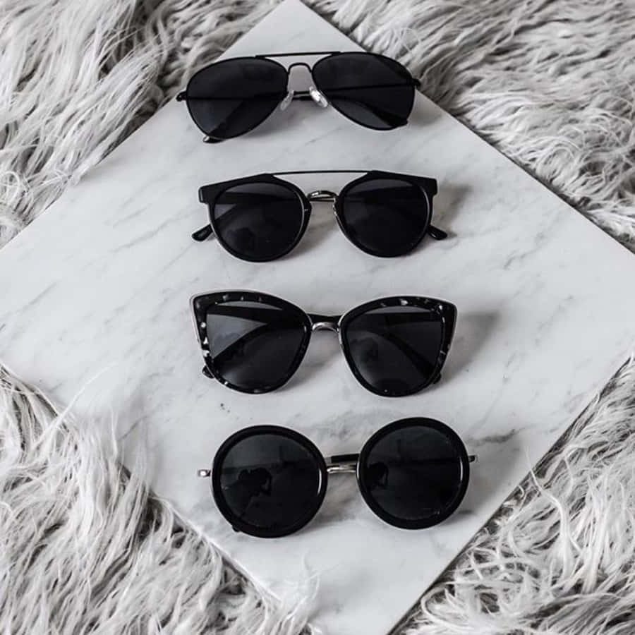 Sunglasses 桌布 壁紙 — 四款時尚黑色太陽眼鏡整齊地排列在白色大理石板上，下方是毛絨白色地毯。