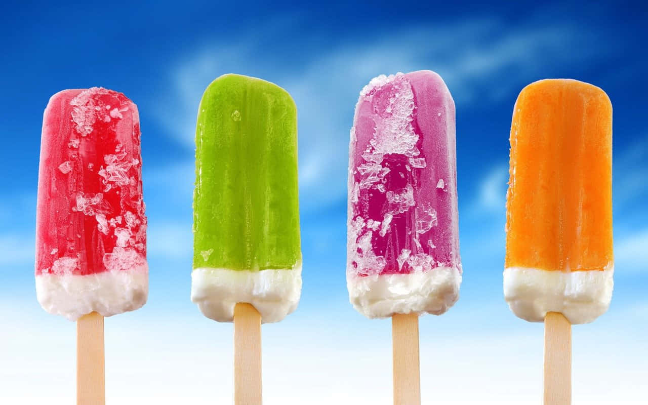 Ice Cream 桌布 壁紙 — 四款色彩繽紛的冰棒，頂部帶有融化的霜狀層，排列成一排，背景是明亮的藍天和柔軟的白雲。