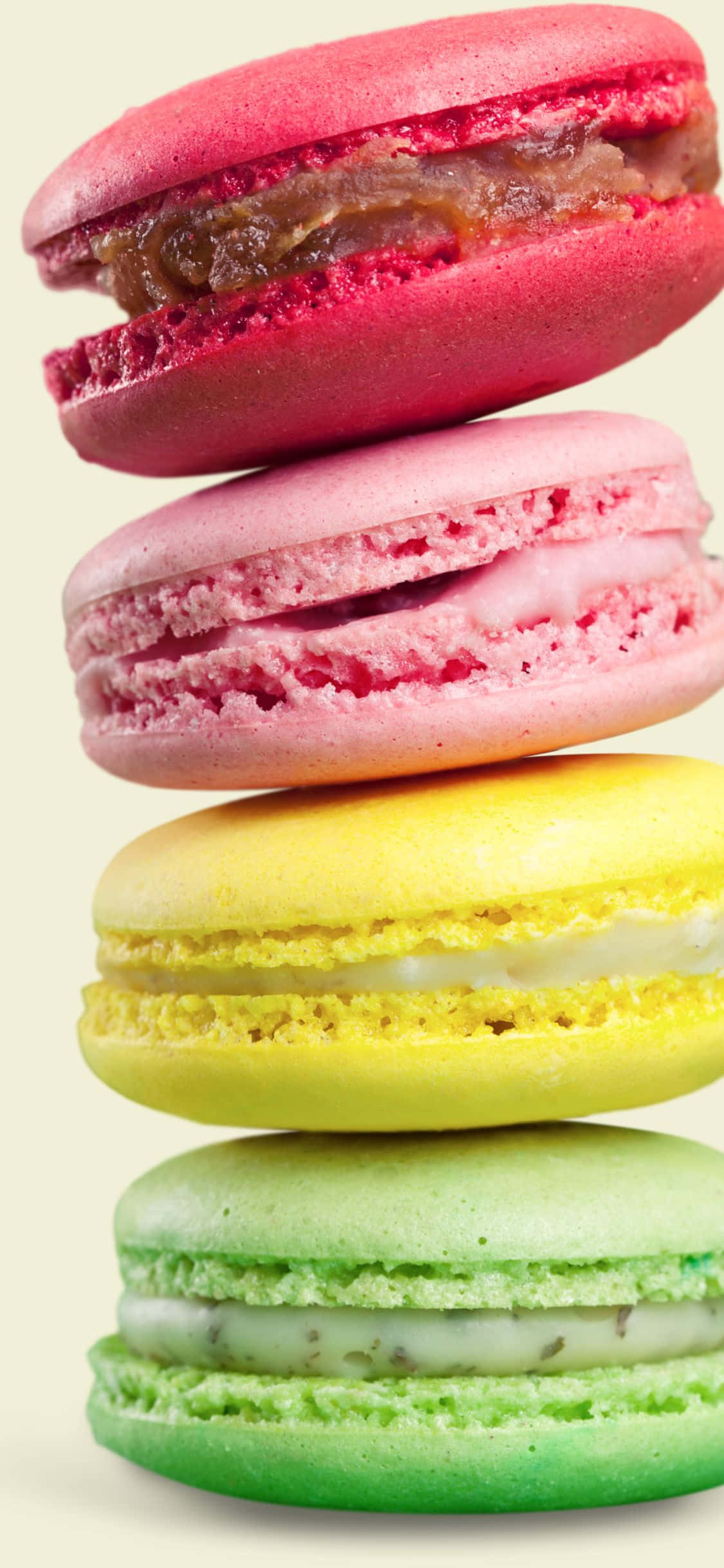 Macarons 桌布 壁紙 — 四款色彩繽紛的馬卡龍（粉紅、黃、綠、紅）堆疊在一起，內餡 creamy，背景是柔和的奶油色。