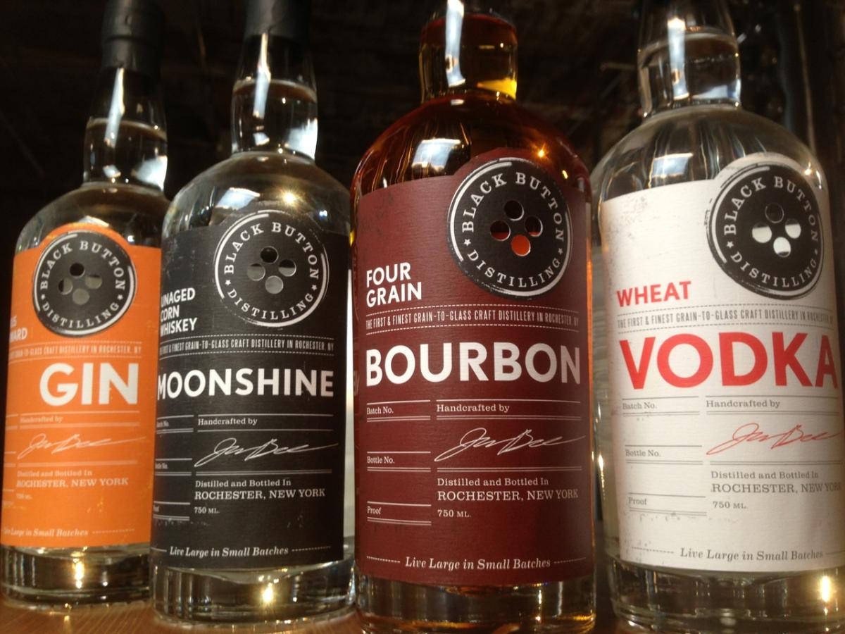 bottle 桌布 壁紙 — 四瓶 Black Button Distilling 酒瓶——琴酒、月光酒、波本威士忌和伏特加——並排而立，標籤醒目，燈光溫暖。