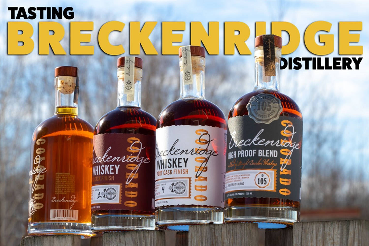 drinks 桌布 壁紙 — 四瓶 Breckenridge Distillery 威士忌排列在木柵欄上，背景是明亮的藍天和模糊的樹木。