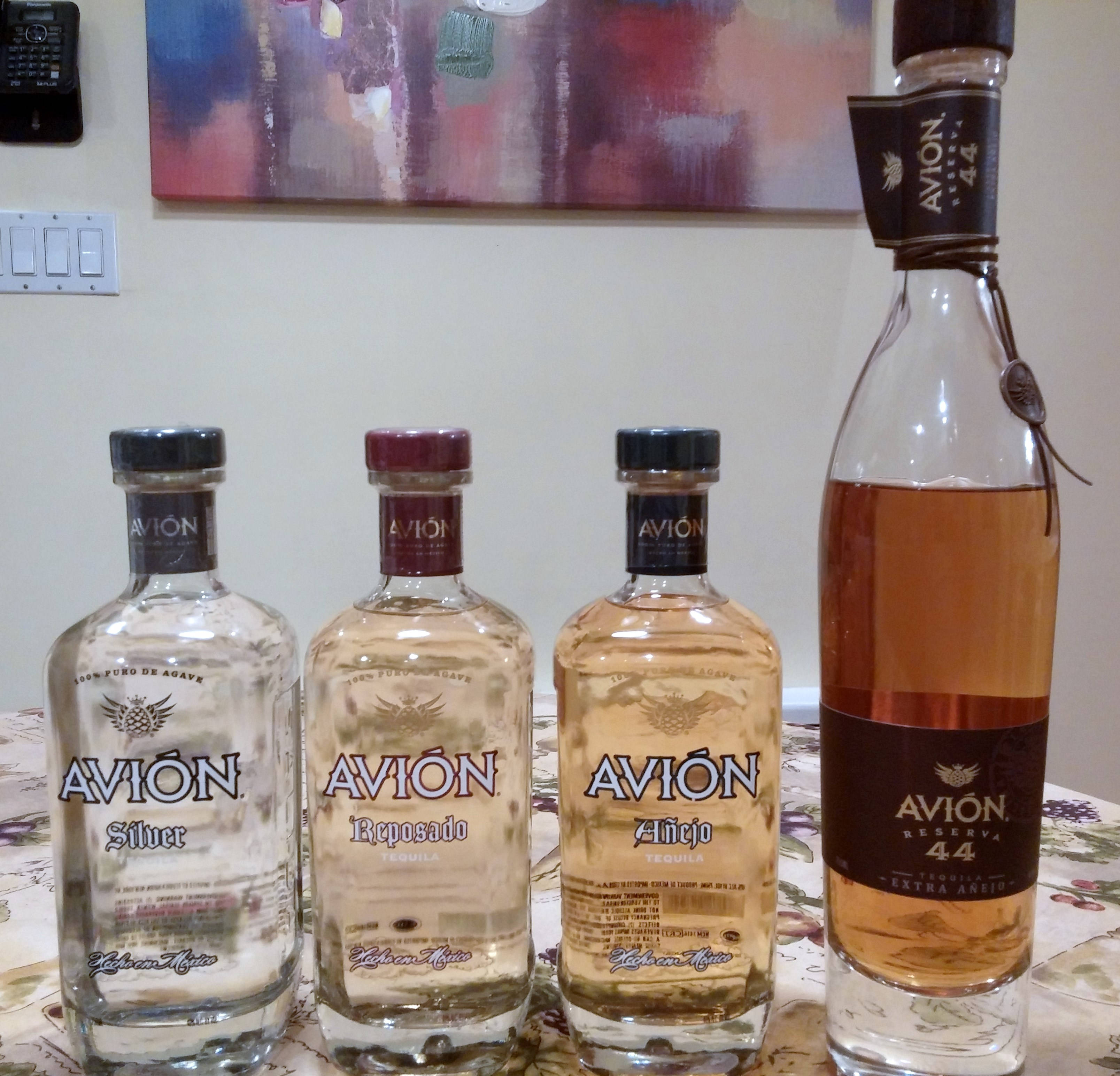 bottle 桌布 壁紙 — 四瓶不同年份的Avion龍舌蘭酒在溫暖的室內燈光下排列在花卉桌布上。