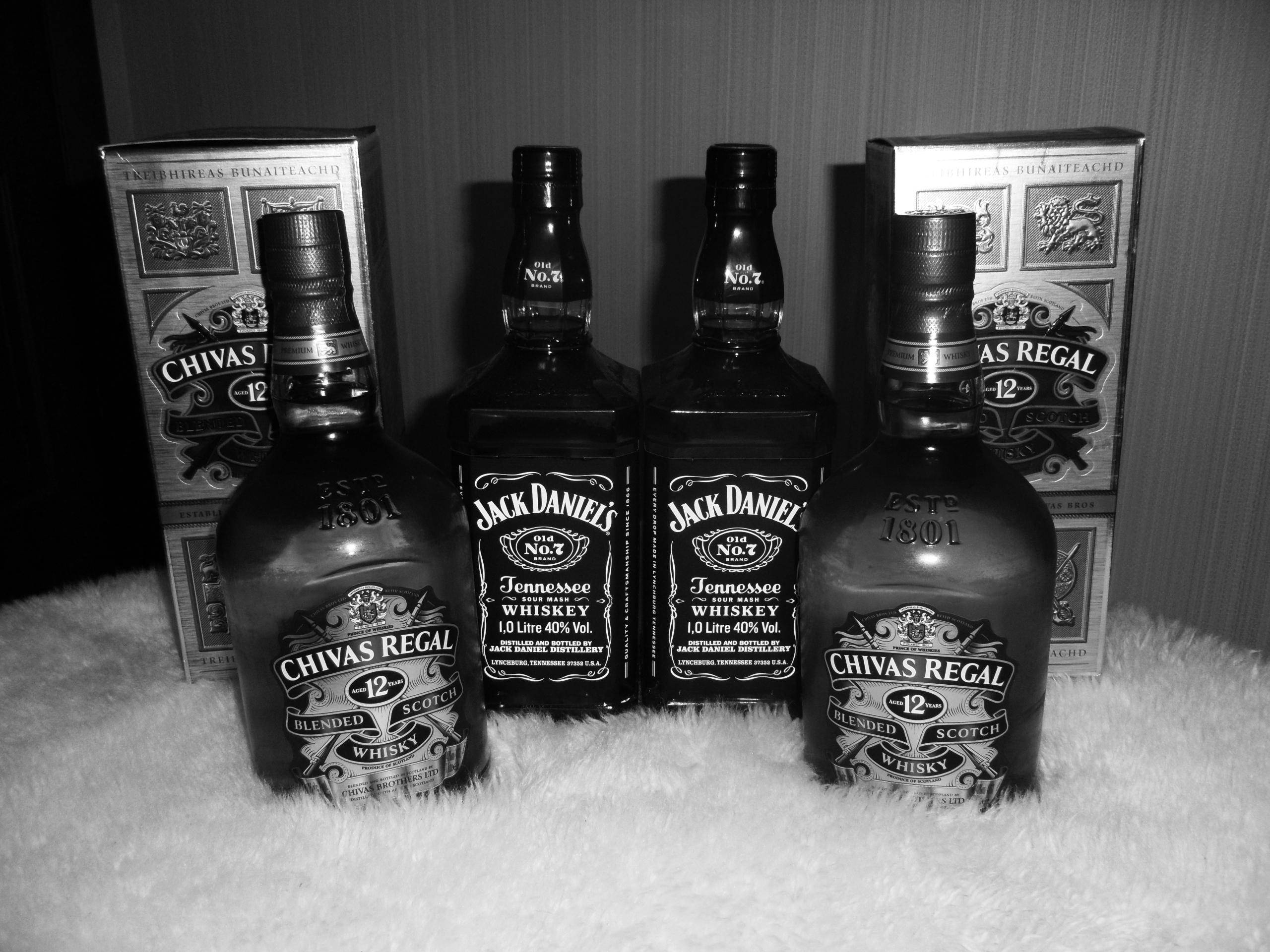 drinks 桌布 壁紙 — 四瓶威士忌，包括芝華士和傑克丹尼，排列在白色毛絨表面上，黑白風格。