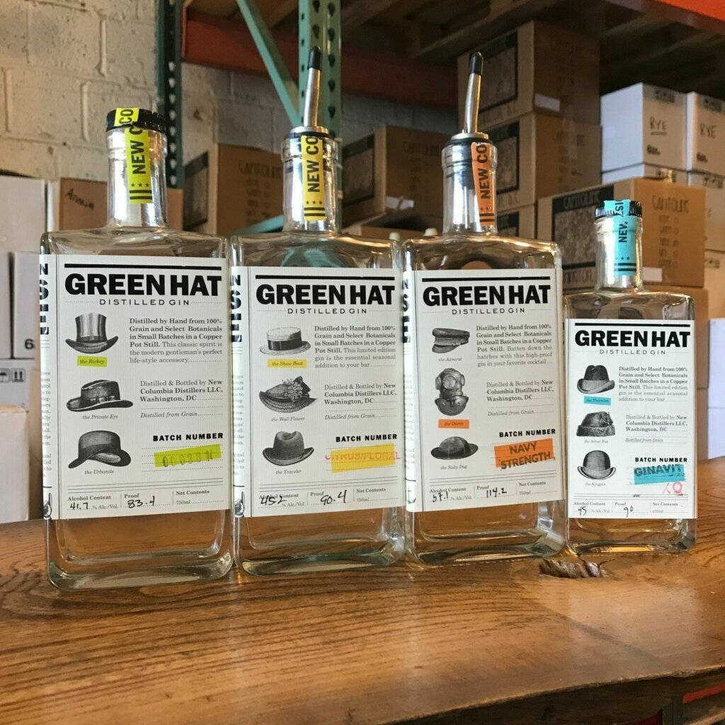 Gin 桌布 壁紙 — 四瓶透明的Green Hat Distilled Gin，帶有獨特帽子主題標籤，放在倉庫環境的木架上。