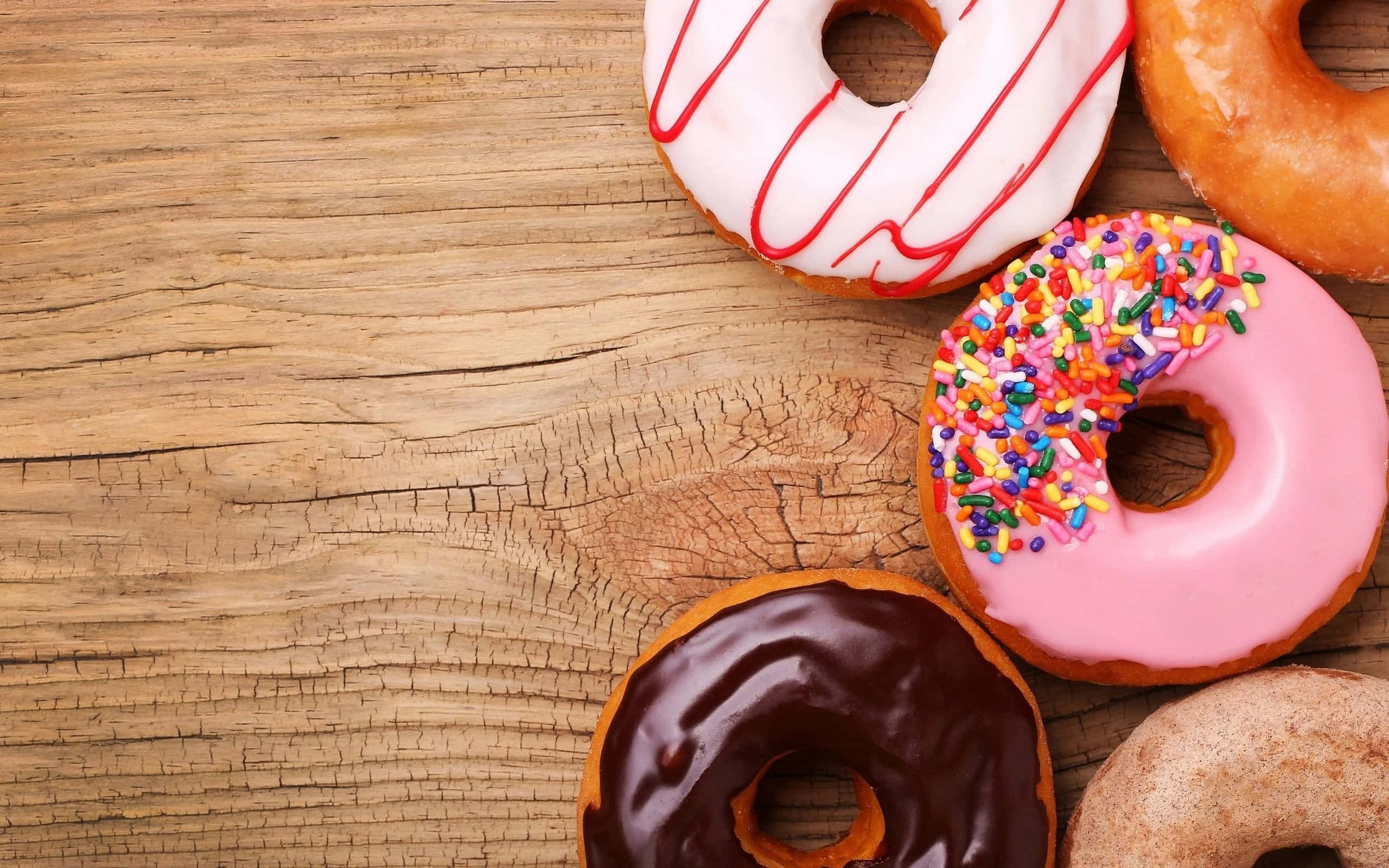 Dunkin Donuts 桌布 壁紙 — 四種不同的釉面甜甜圈，有粉紅色糖針、紅色淋醬和巧克力糖霜，放在鄉村風格的木質表面上。
