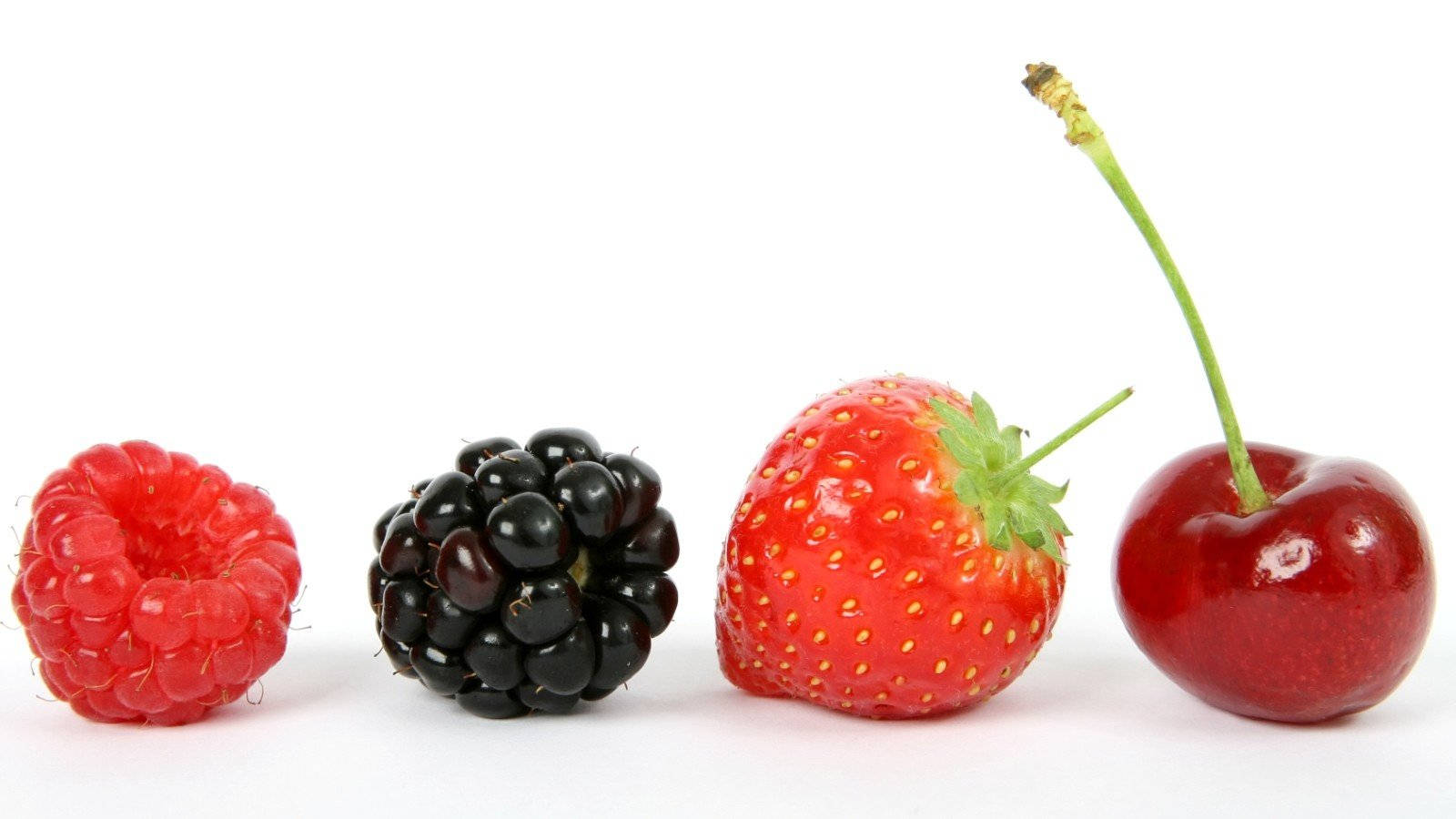 Berry 桌布 壁紙 — 四種鮮豔的新鮮漿果：覆盆子、黑莓、草莓和櫻桃，整齊地排列在乾淨的白色表面上。