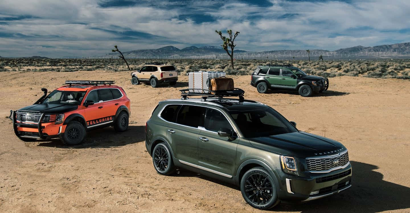 Kia Telluride 桌布 壁紙 — 四輛堅固的SUV配備車頂行李架，停放在廣闊的沙漠景觀中，天空部分多雲。