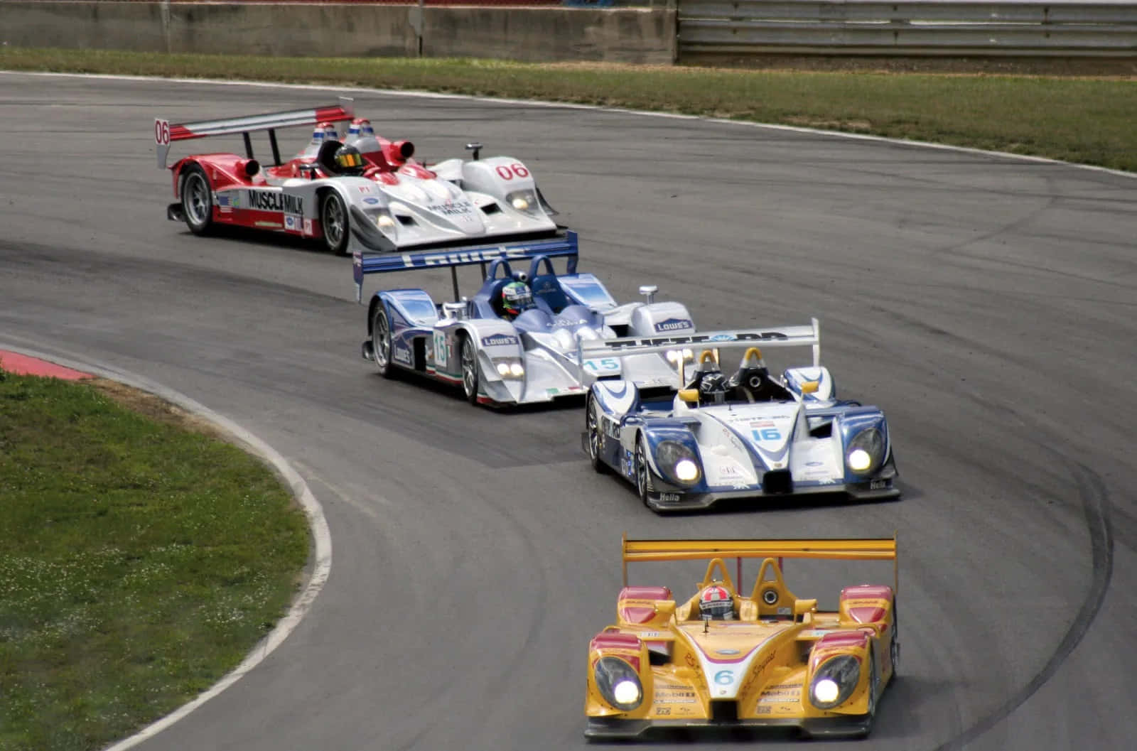 Car Racing 桌布 壁紙 — 四輛流線型賽車在由草地和混凝土護欄圍繞的瀝青賽道上急轉彎。
