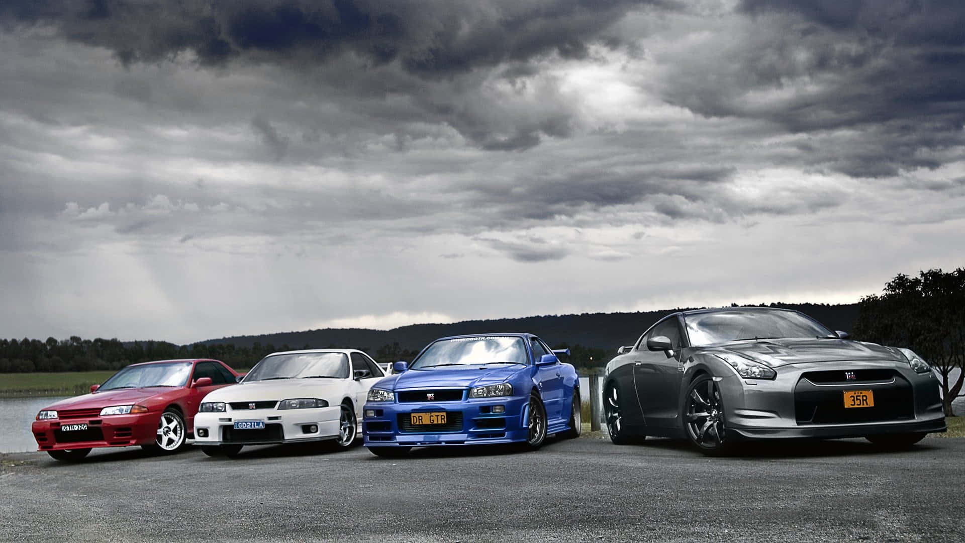 Nissan Skyline 桌布 壁紙 — 四輛高性能跑車，分別為紅色、白色、藍色和銀色，在戲劇性的暴風雨天空下排成一列。