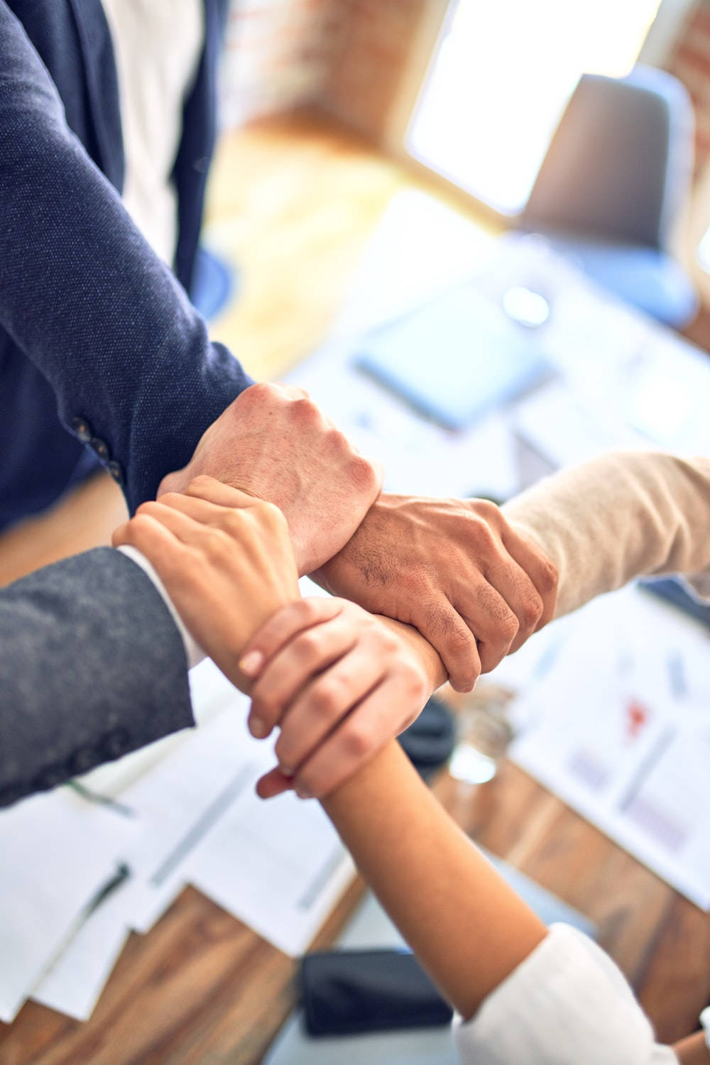Teamwork 桌布 壁紙 — 四隻不同的手在木桌上交疊，桌上放有文件和筆記型電腦，形成團隊圍圈。