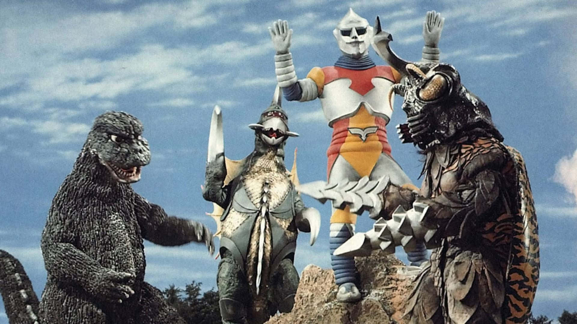 Godzilla Vs Megalon 桌布 壁紙 — 四隻巨型怪獸和一位英雄站在岩石地形上，天空多雲，經典特攝場景。