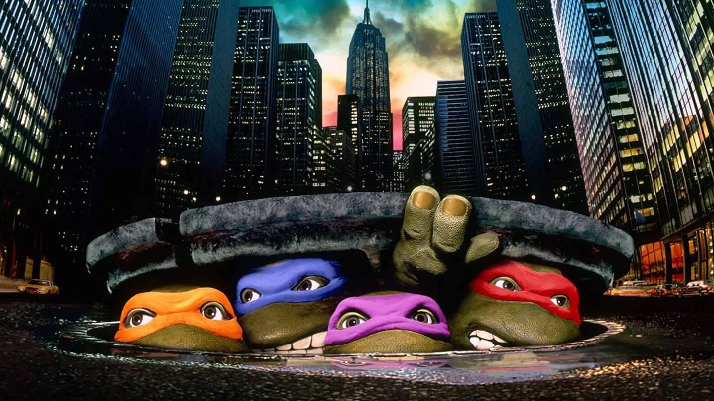 Ninja Turtle 桌布 壁紙 — 四隻忍者龜在黃昏的霓虹燈城市景觀中，從一個人孔蓋探出頭來。