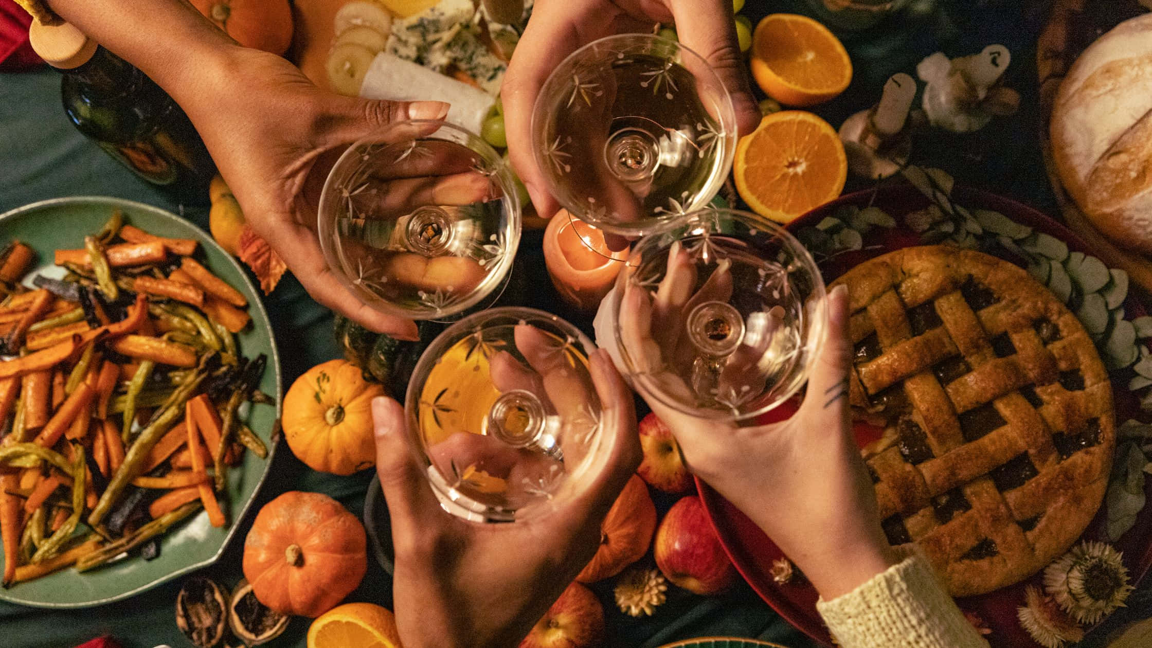 Thanksgiving Desktop 桌布 壁紙 — 四隻手在擺滿派、烤蔬菜、南瓜和柳橙的節日秋季餐桌上碰杯。