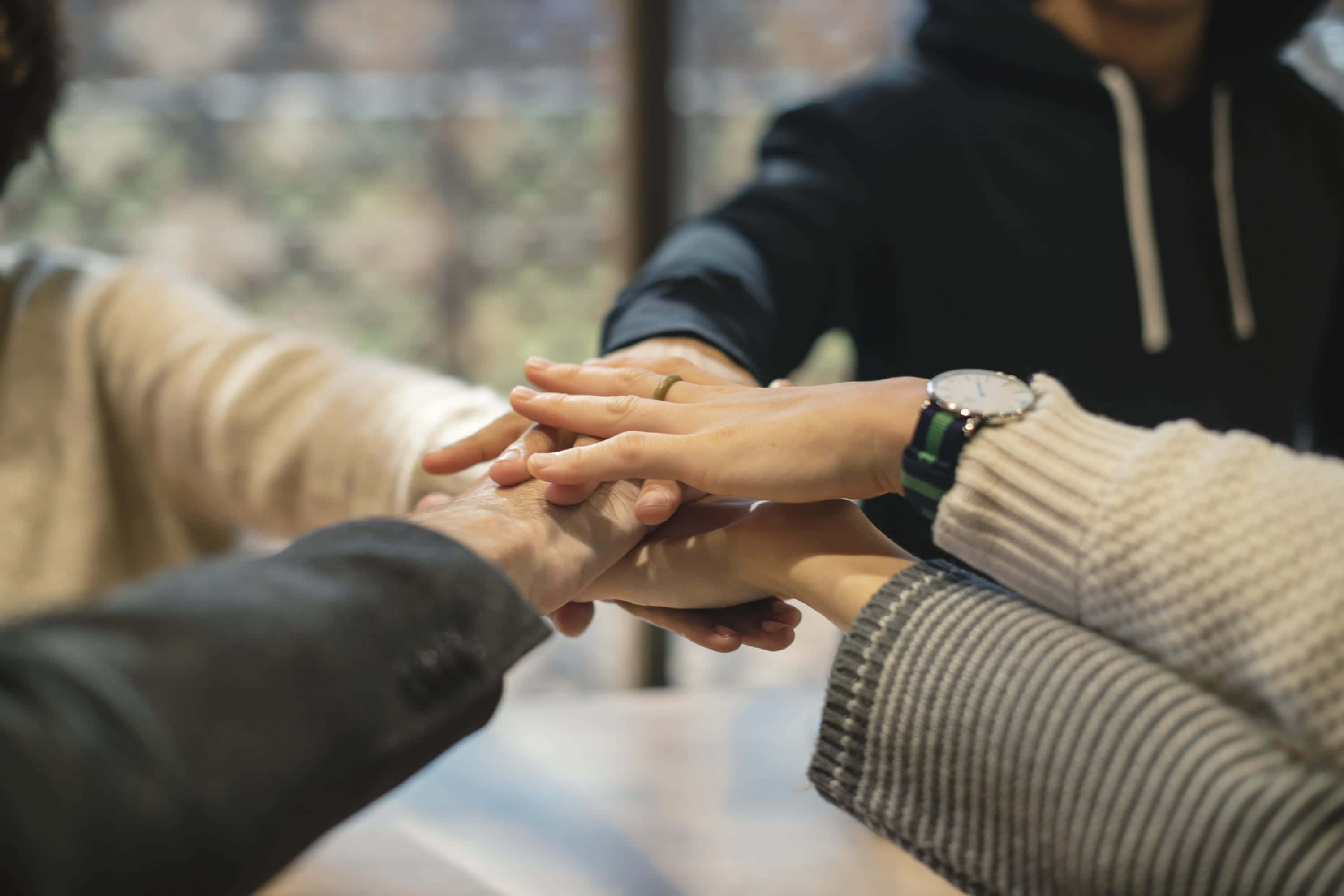 Team 桌布 壁紙 — 四隻手在窗邊的木桌上以支持的手勢疊在一起。