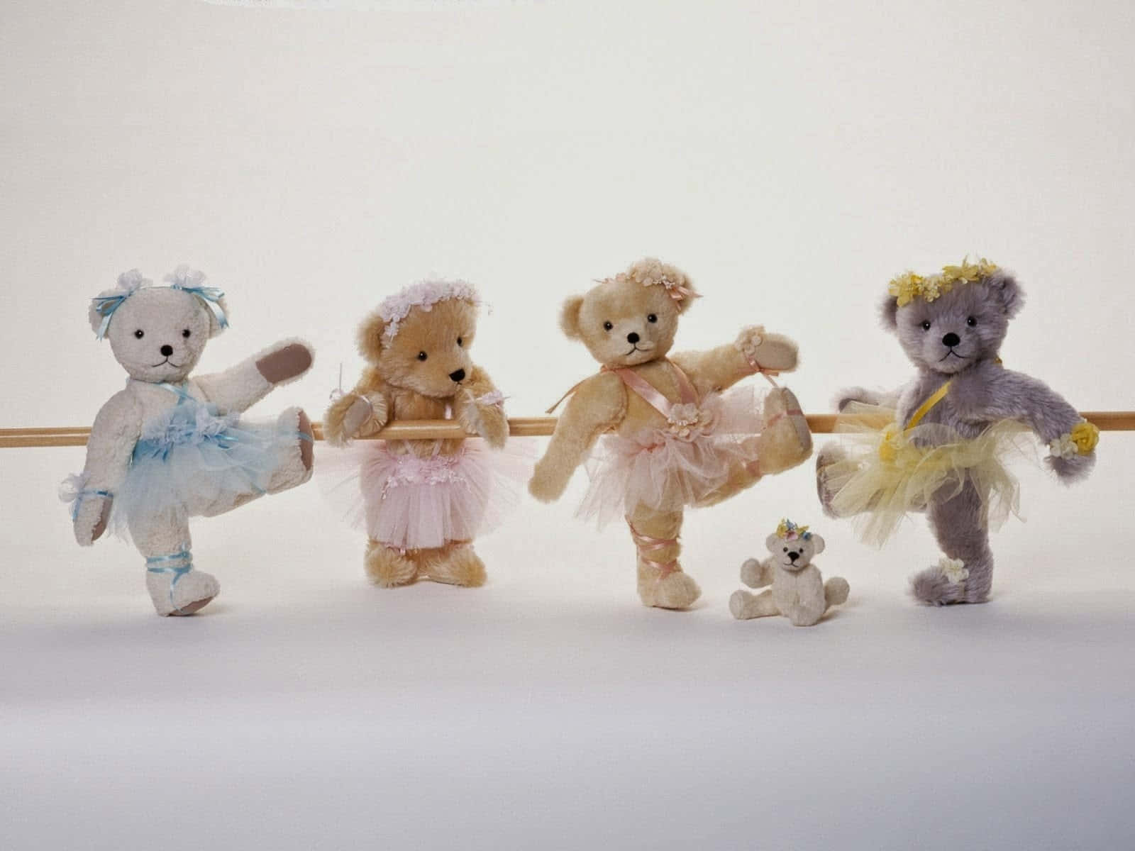 Teddy Bear 桌布 壁紙 — 四隻穿著粉彩芭蕾舞服裝的泰迪熊在明亮的工作室地板上擺出優雅的姿勢，附近坐著一隻小熊。