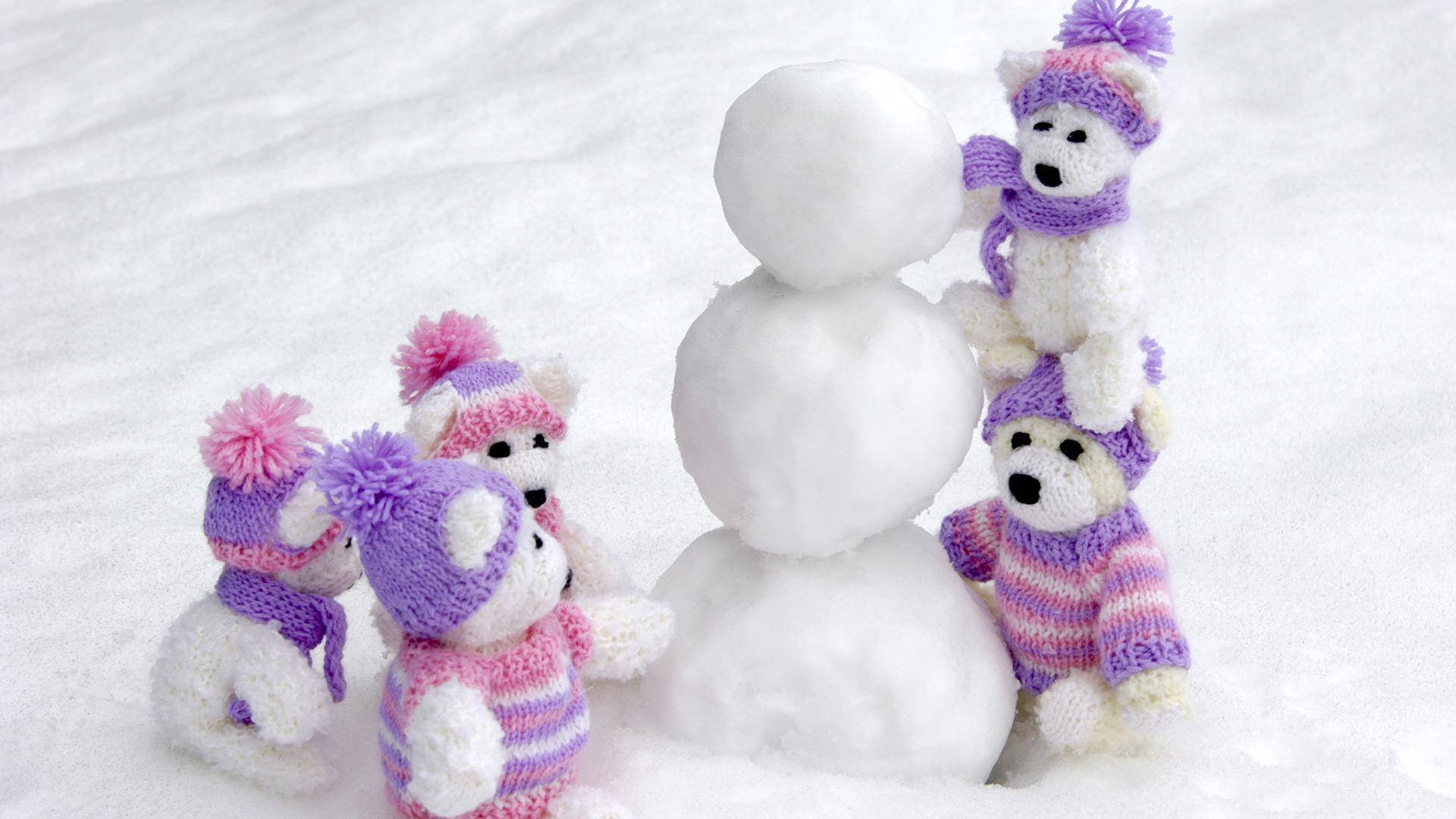 Teddy Bear 桌布 壁紙 — 四隻穿著紫粉色帽子和圍巾的編織泰迪熊在雪地裡圍著一個雪人。