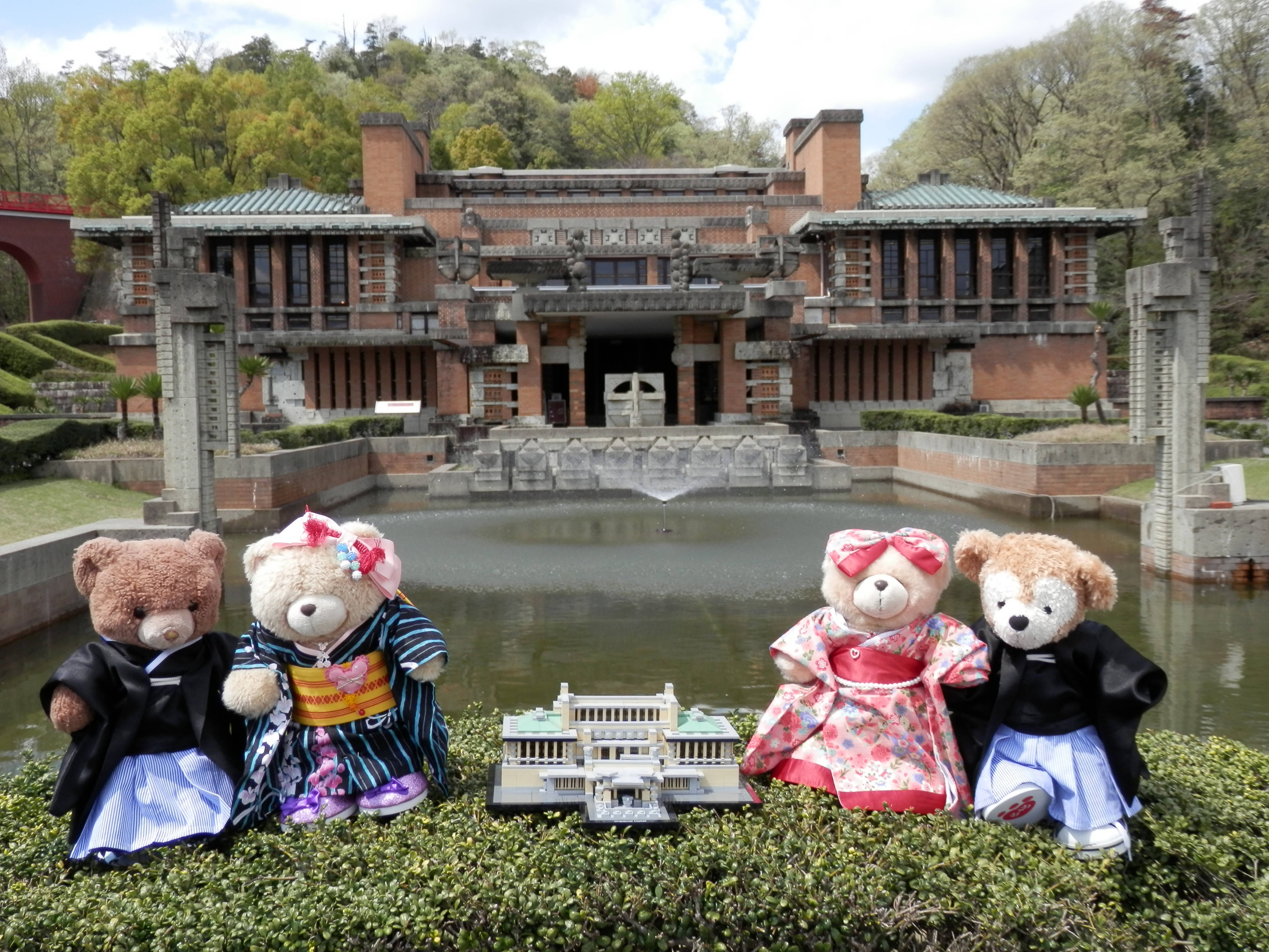 Nagoya 桌布 壁紙 — 四隻穿著色彩繽紛和服的泰迪熊坐在草地上，面前是一座倒映在水中的宏偉日本建築的微型複製品。