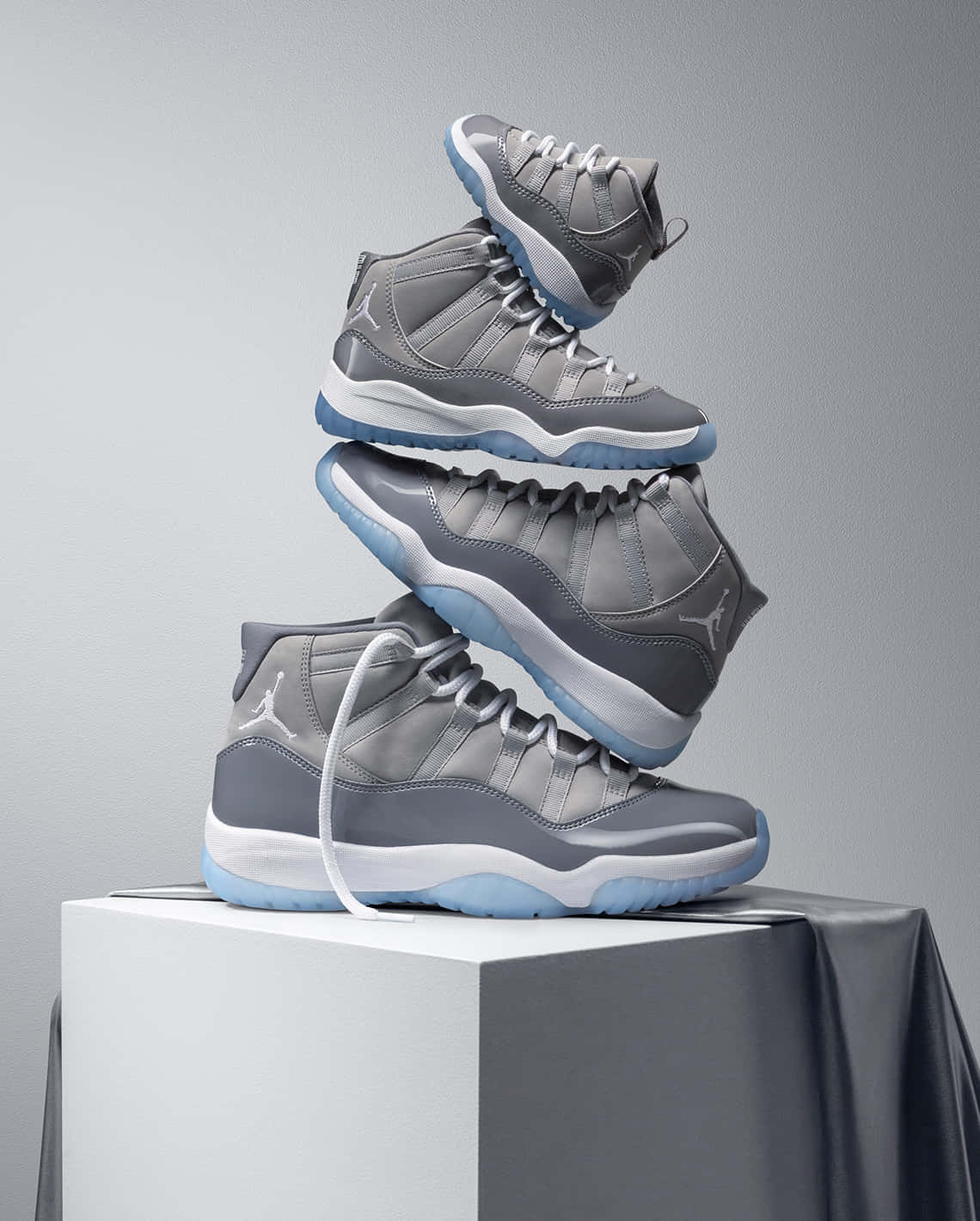 Cool Grey 桌布 壁紙 — 四雙灰色 Jordan 11 運動鞋以金字塔形狀堆疊在白色底座上，背景為中性灰色。
