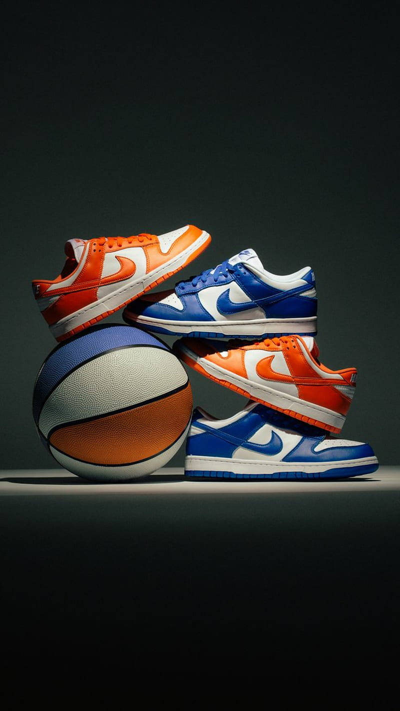 Nike Shoes 桌布 壁紙 — 四雙鮮豔的橙色和藍色Nike Dunk運動鞋堆疊在籃球周圍，背景為深色攝影棚。