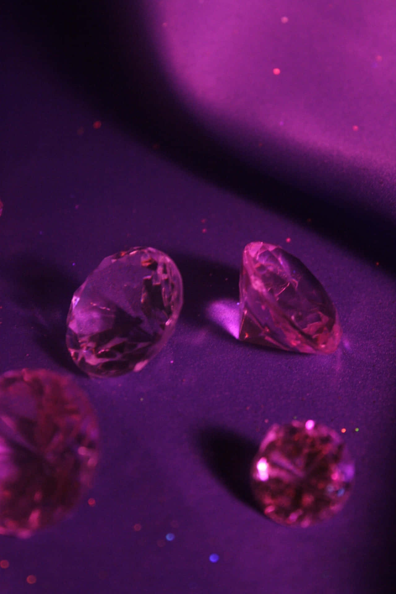 Diamond Aesthetic 桌布 壁紙 — 四顆刻面粉紅寶石在紫色燈光下，於閃閃發光的天鵝絨表面上閃爍。