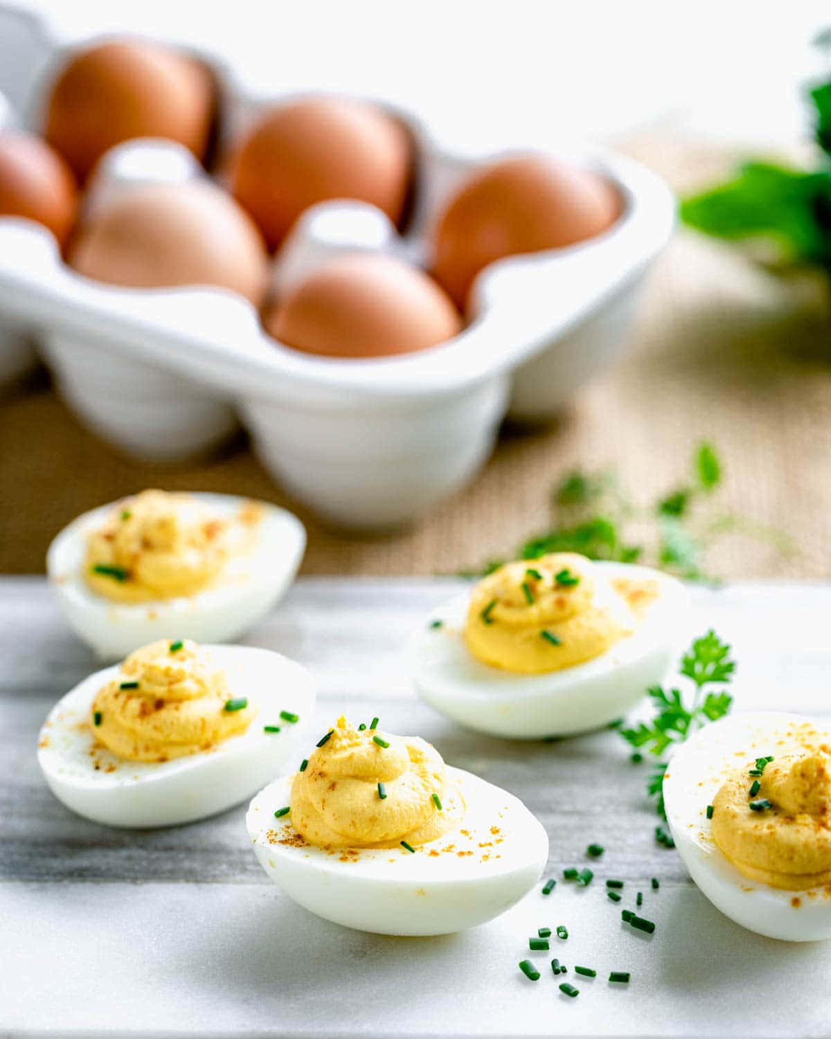 Eggs 桌布 壁紙 — 四顆惡魔蛋（Deviled eggs）以細香蔥點綴，放在大理石檯面上，後方有一盒棕色雞蛋呈現柔焦效果。