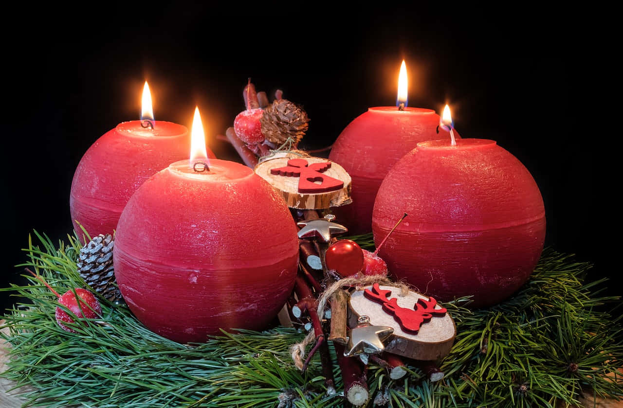 Advent 桌布 壁紙 — 四顆發光的紅色球形蠟燭，藏在綠色松針中，搭配節日木製裝飾，背景為黑色。