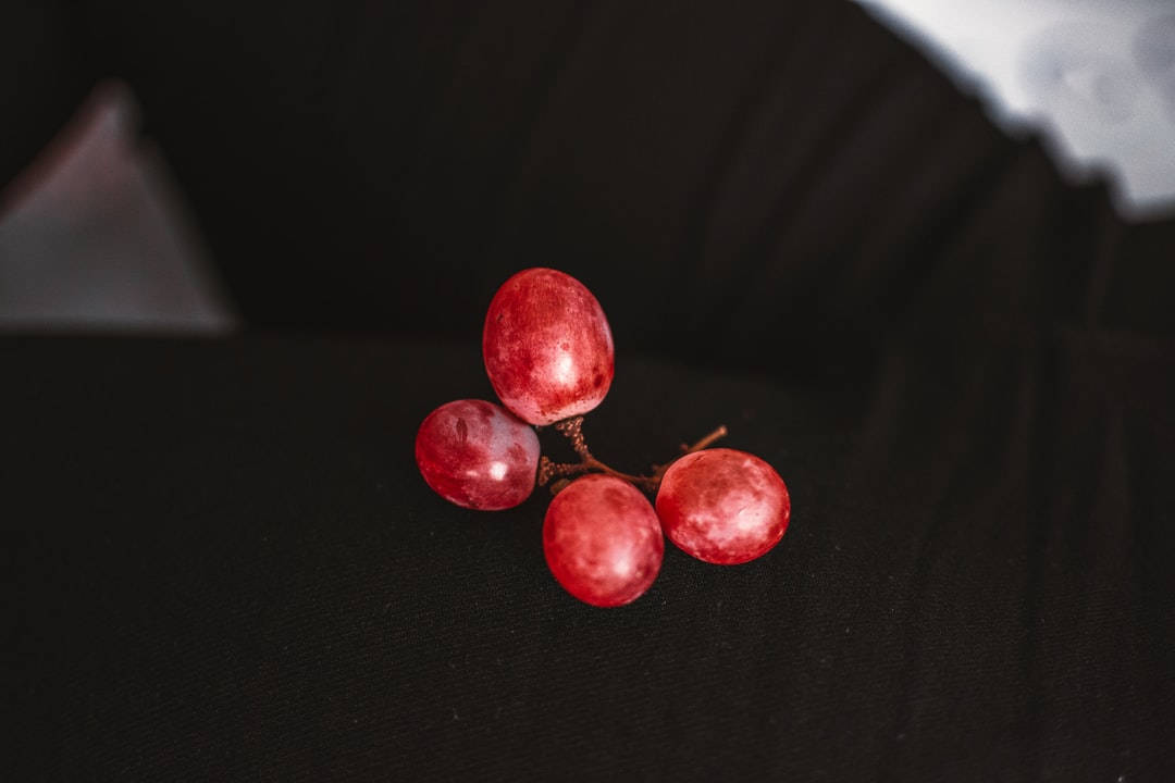 Grape 桌布 壁紙 — 四顆飽滿的紅葡萄在柔和的燈光下，在深色紋理表面上閃閃發光。