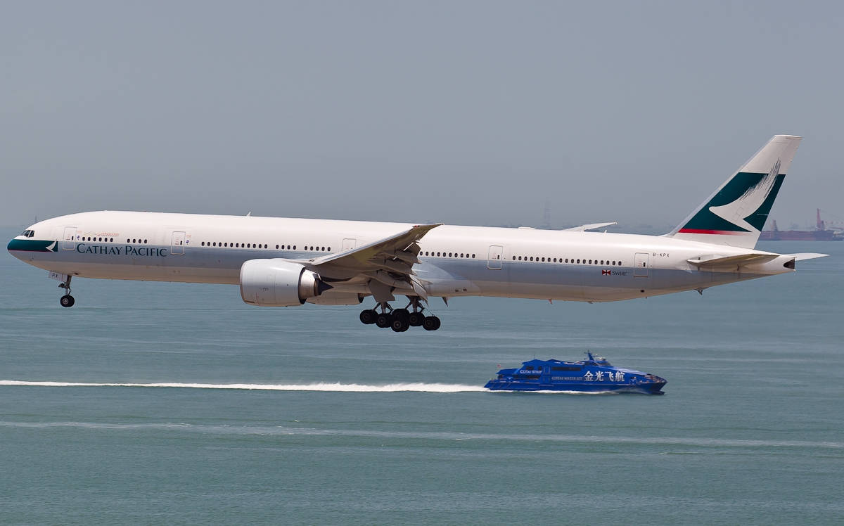 船 桌布 壁紙 — 國泰航空飛機低飛過碧綠海水，藍色快艇在其下方疾馳。