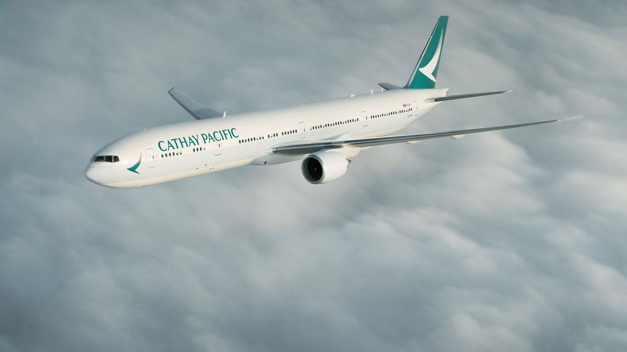 飛機 桌布 壁紙 — 國泰航空飛機在晴朗天空中優雅地翱翔於一層柔軟的灰色雲層之上。
