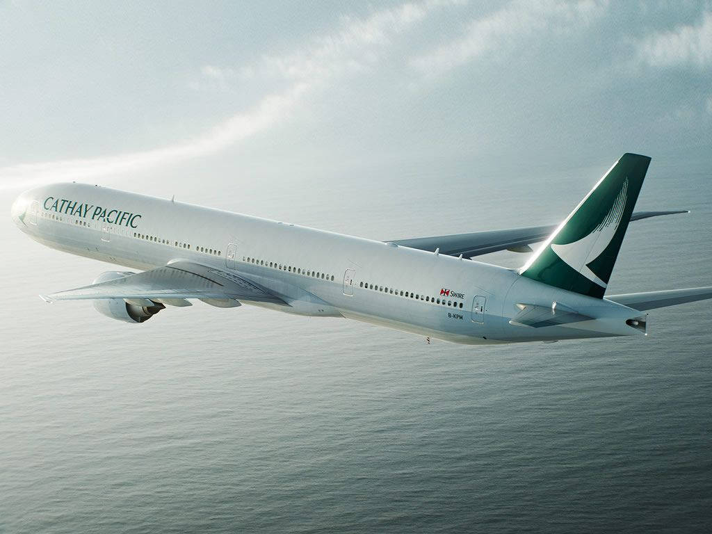 飛機 桌布 壁紙 — 國泰航空飛機在柔和的多雲天空下，優雅地翱翔於平靜的海面上。