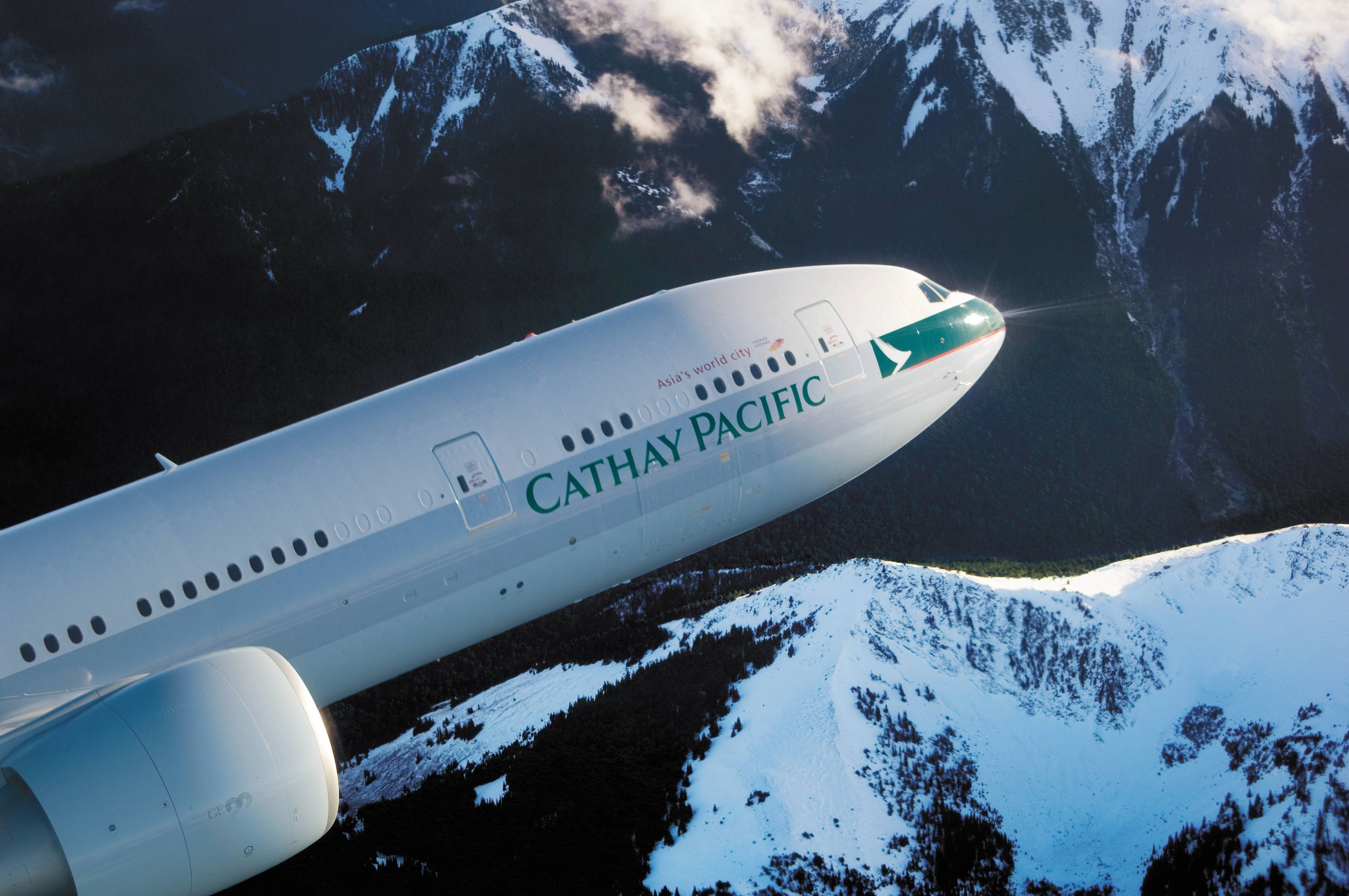 飛機 桌布 壁紙 — 國泰航空飛機在白雪覆蓋的山峰上空翱翔，陽光在機身上閃閃發光。