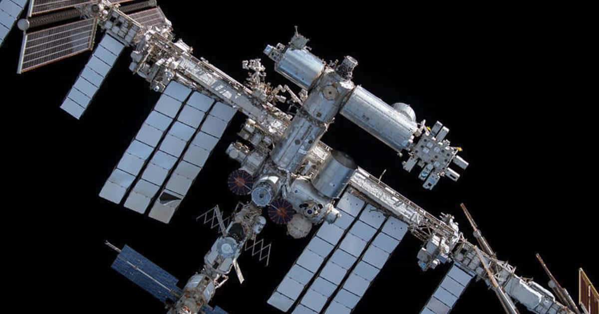 International Space Station 桌布 壁紙 — 國際太空站漂浮在漆黑的太空中，太陽能板伸展，面對太空的虛無。